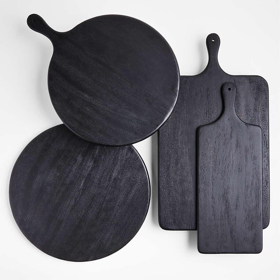 Set of four black oak cutting and butter boards, two round and two rectangular with handles and hanging holes, arranged overlapping on a white background showing smooth dark wood grain and a matte finish.