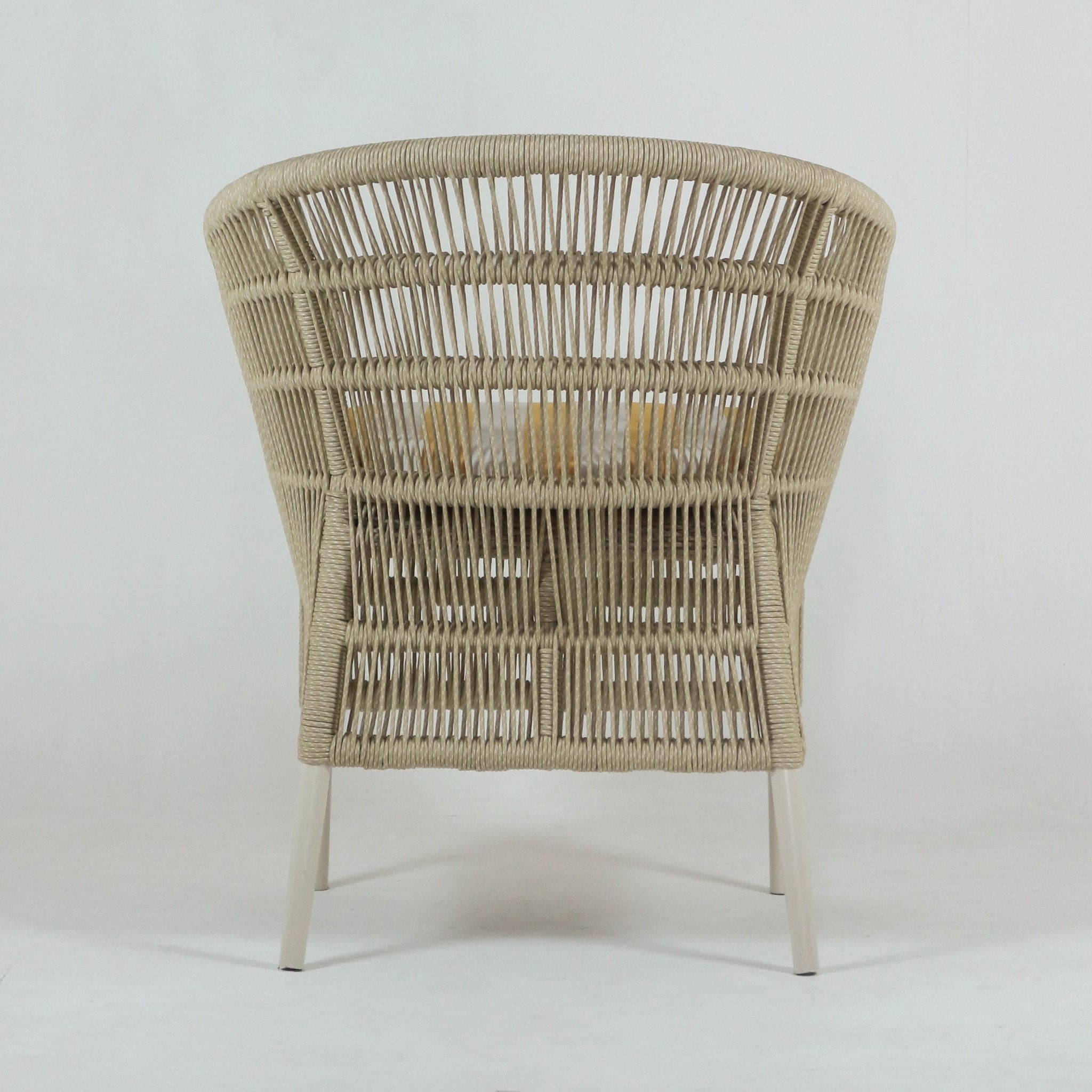 Rear view of a coastal outdoor patio chair with light beige woven rope back, white metal legs and a weather-resistant cushioned seat with a yellow accent pillow visible through the weave.