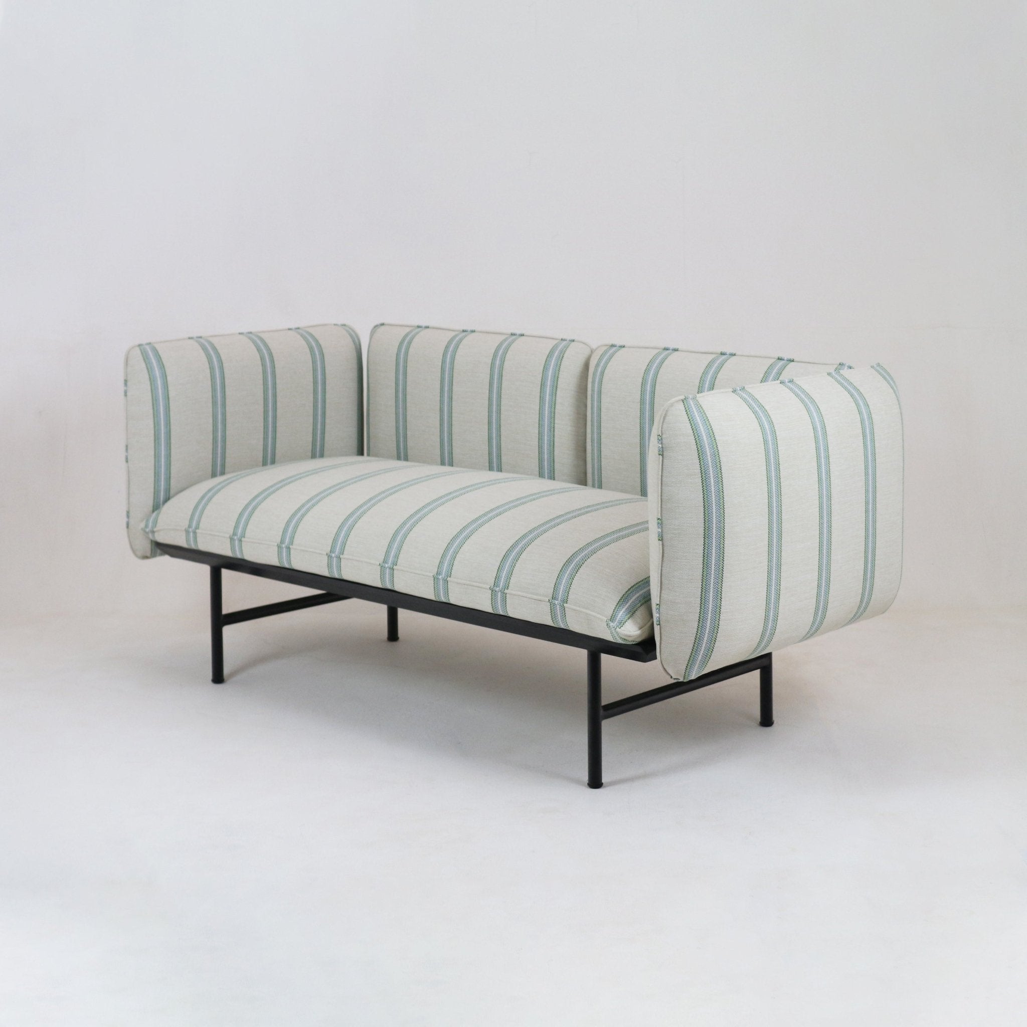 Cream fabric-upholstered outdoor sectional sofa with vertical seafoam-green stripes, squared boxed arms and low black metal frame legs in a coastal-modern style, photographed on a neutral studio background.