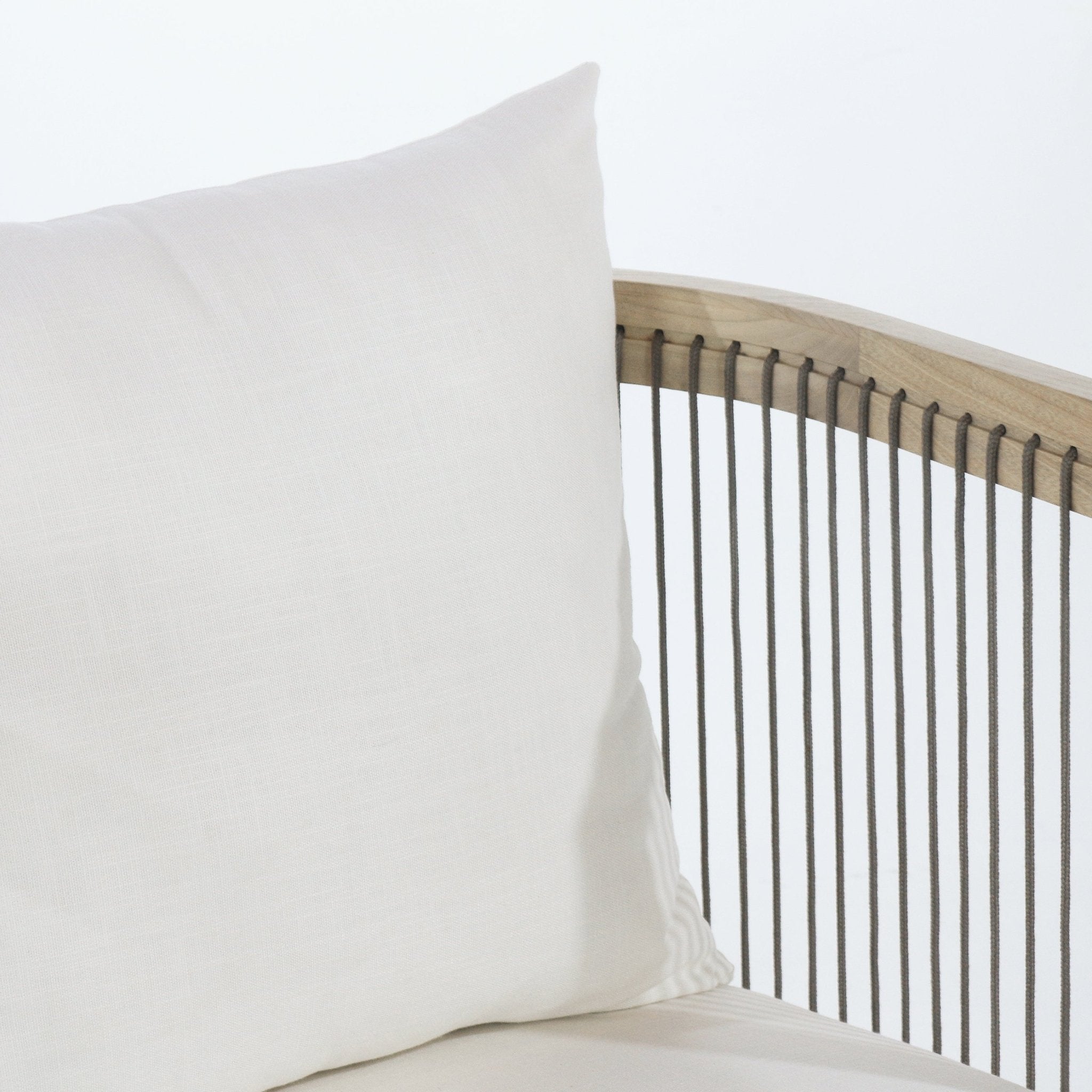 Close-up of a white linen cushion on a dining chair, showing the curved natural wood back rail with evenly spaced brown rope cords and a portion of the neutral seat cushion.