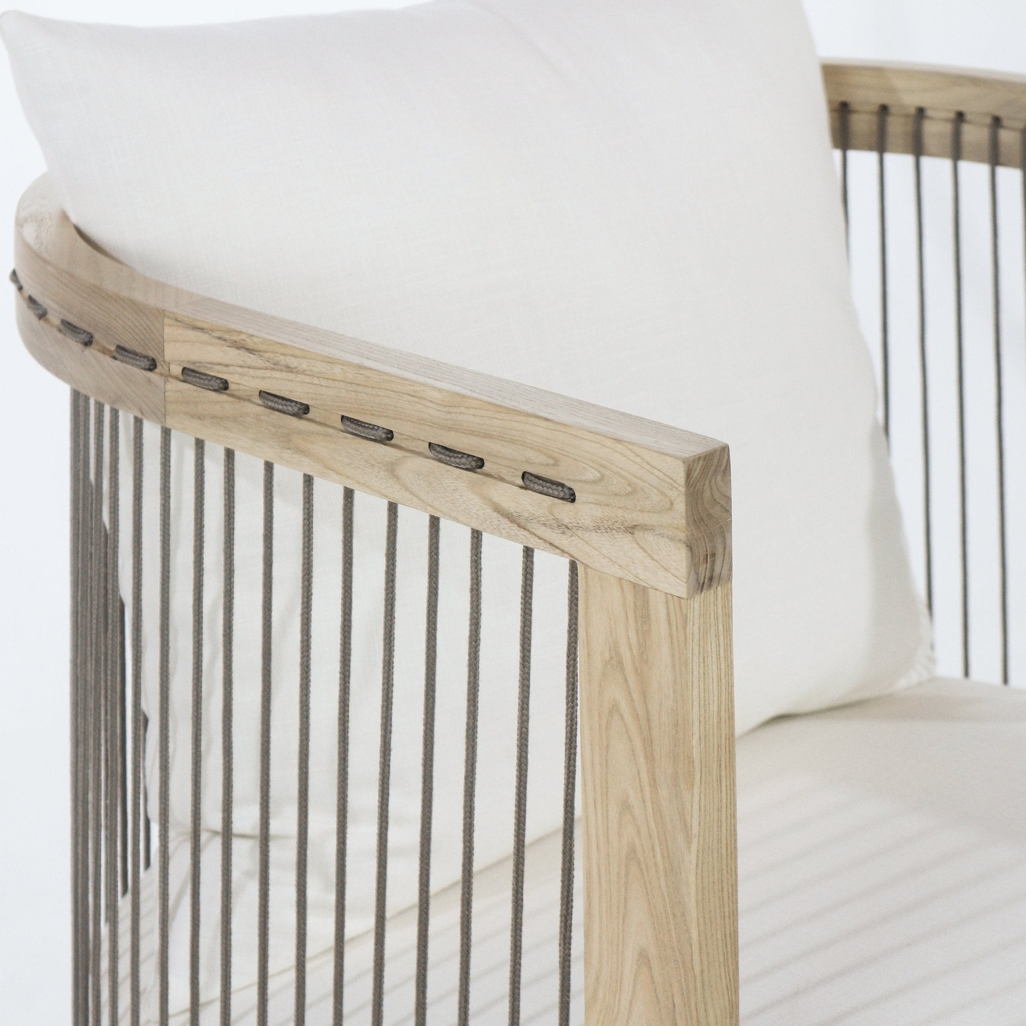 Close-up of a dining chair armrest in white oak showing light natural wood grain, vertical gray rope spindles and a white fabric cushion for a modern Scandinavian look.