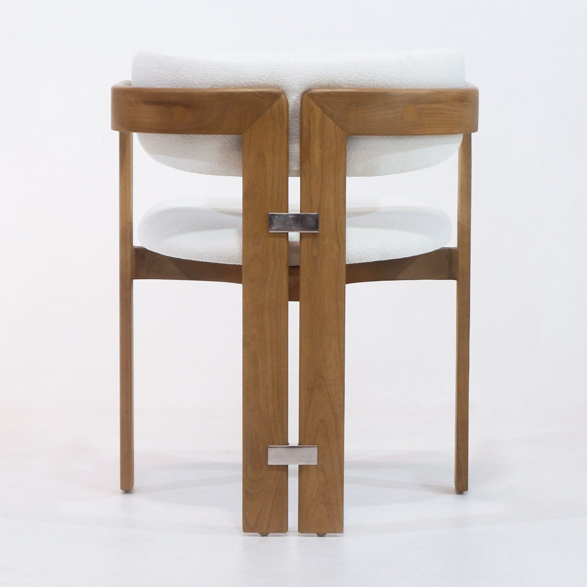 Rear view of a mid-century modern dining chair with a teak wood frame, white boucle upholstered seat and back, and rectangular stainless-steel connectors joining the split rear legs.