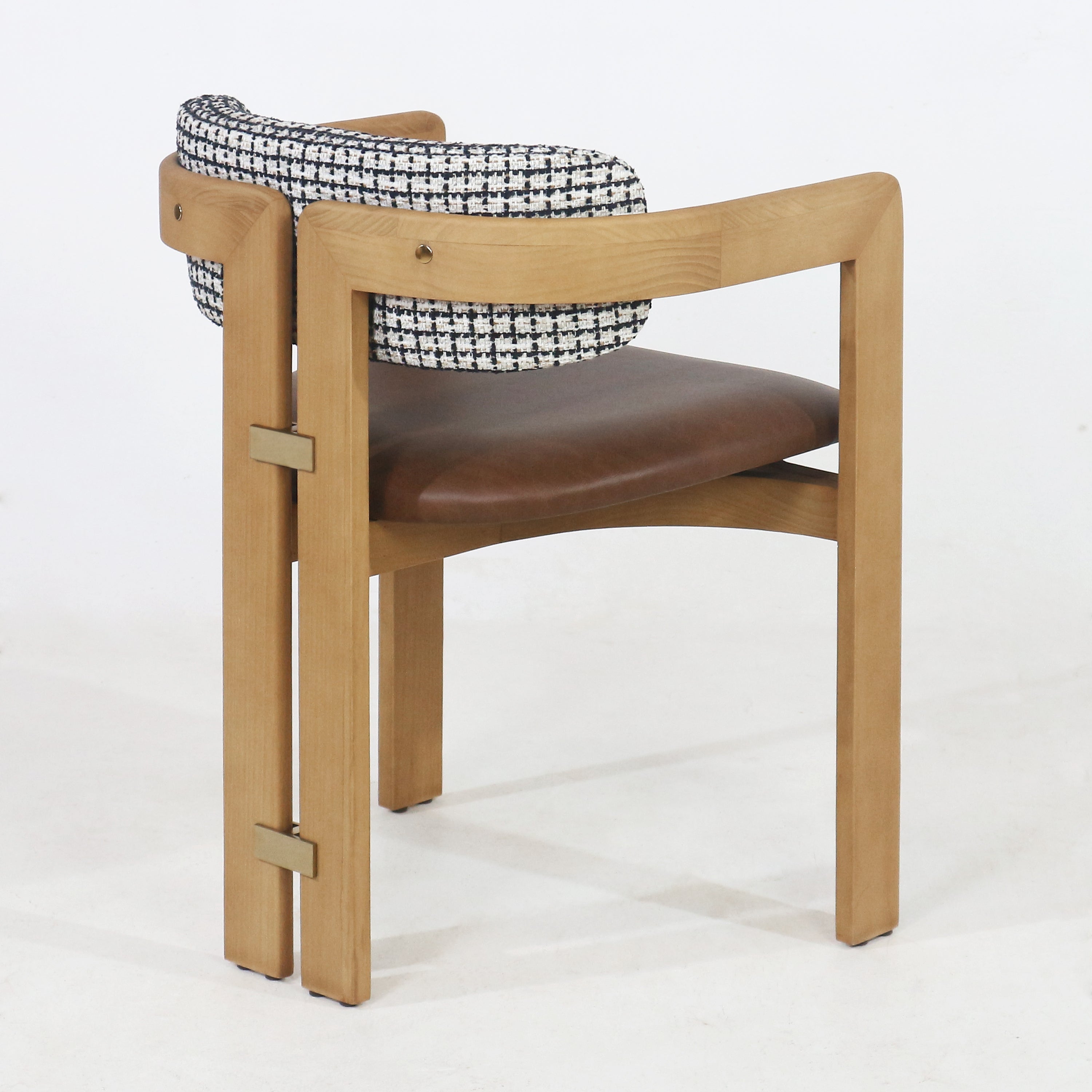 Rear three-quarter view of a teak dining chair with a light teak wood frame, black-and-white tweed back cushion, brown leather-upholstered seat and subtle brass accent hardware on the leg.