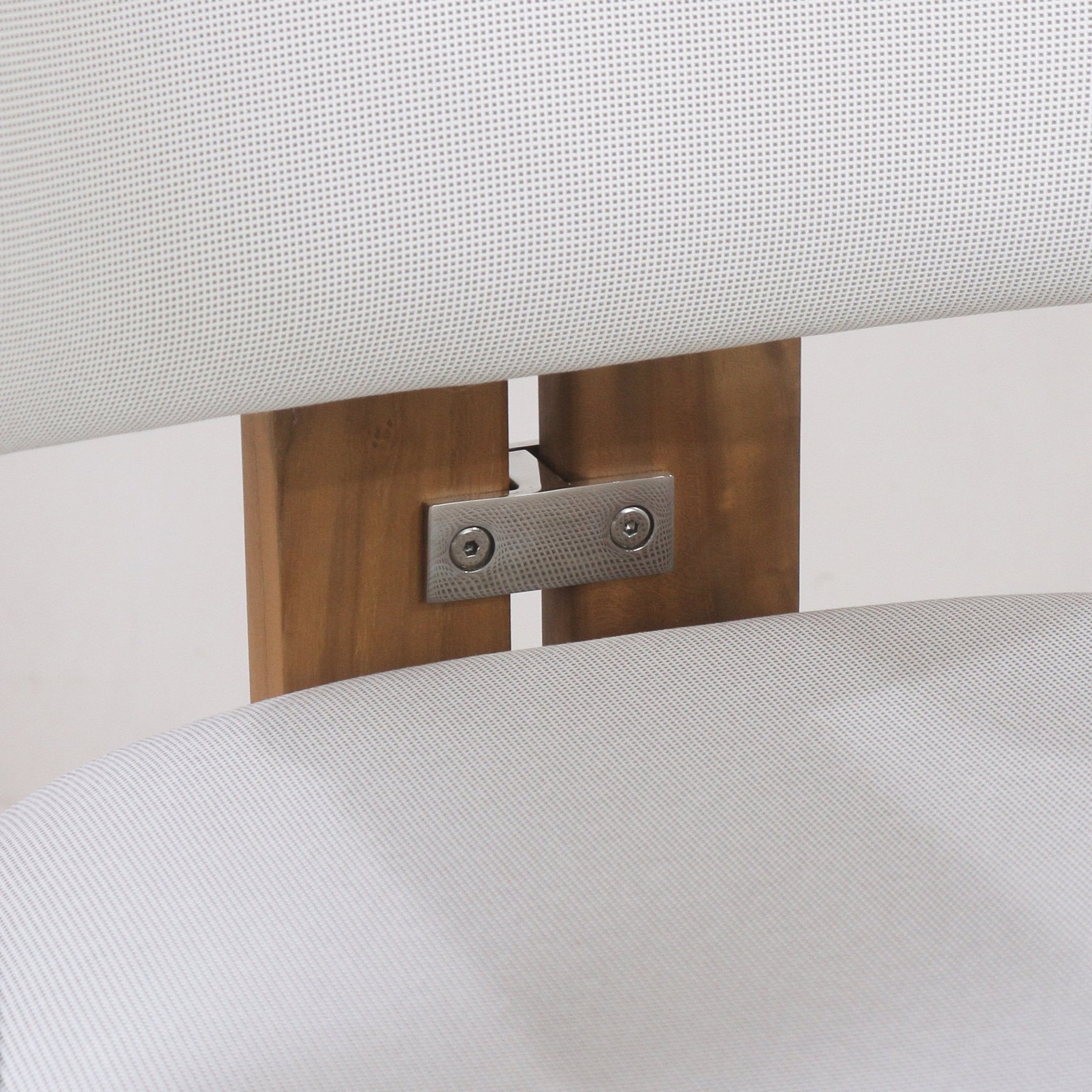 Close-up of a teak outdoor bar stool back showing a stainless steel bracket with two screws fastening warm teak slats to white textured outdoor fabric on the seat and back.