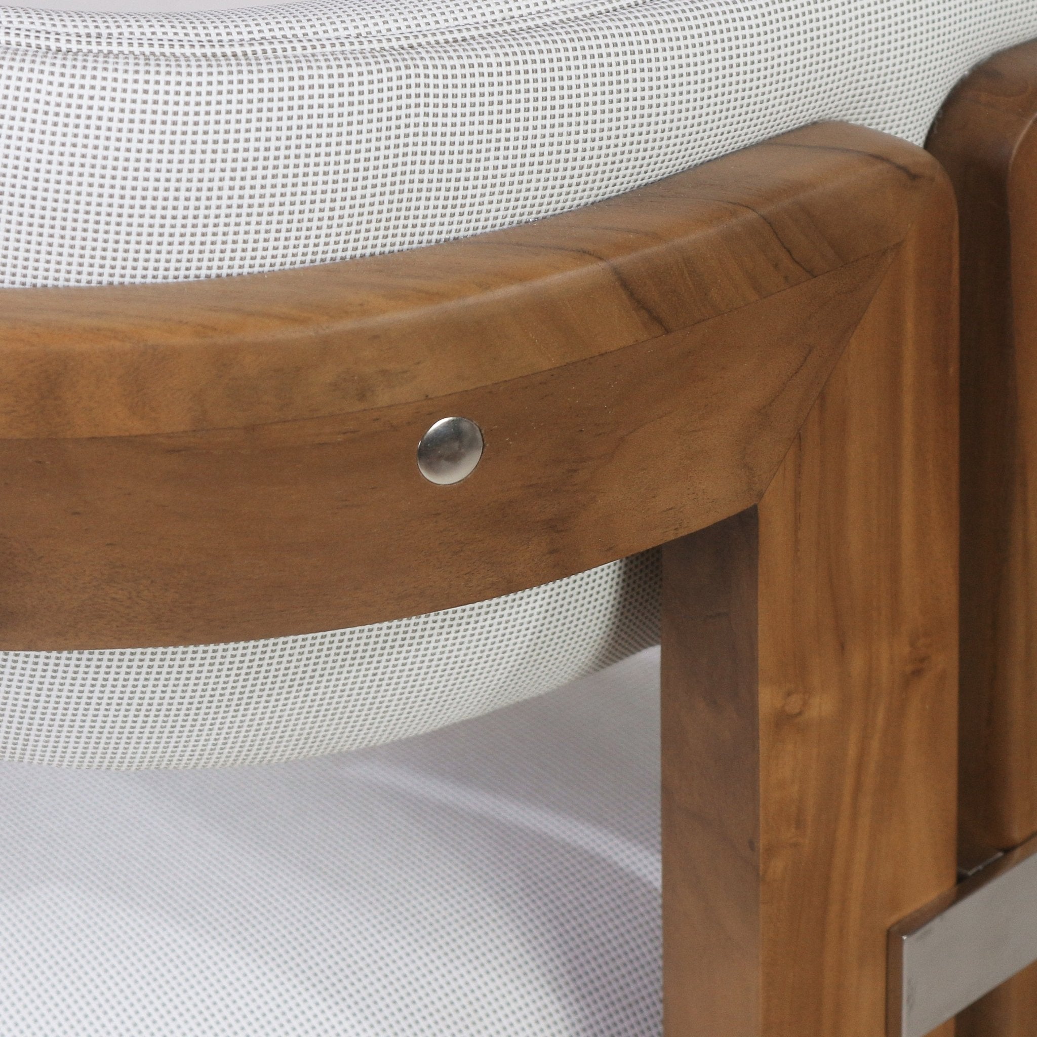 Close-up of a teak bar stool back showing the warm grained teak frame, white textured outdoor fabric upholstery, and a round stainless-steel fastener on the curved back support.