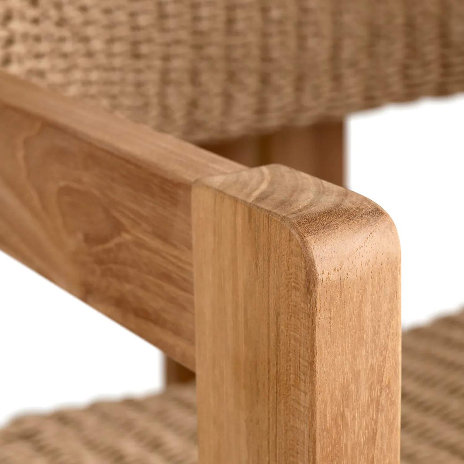 Close-up of a natural teak armrest with rounded corner and visible wood grain, with beige woven synthetic seat and back in soft focus behind it.
