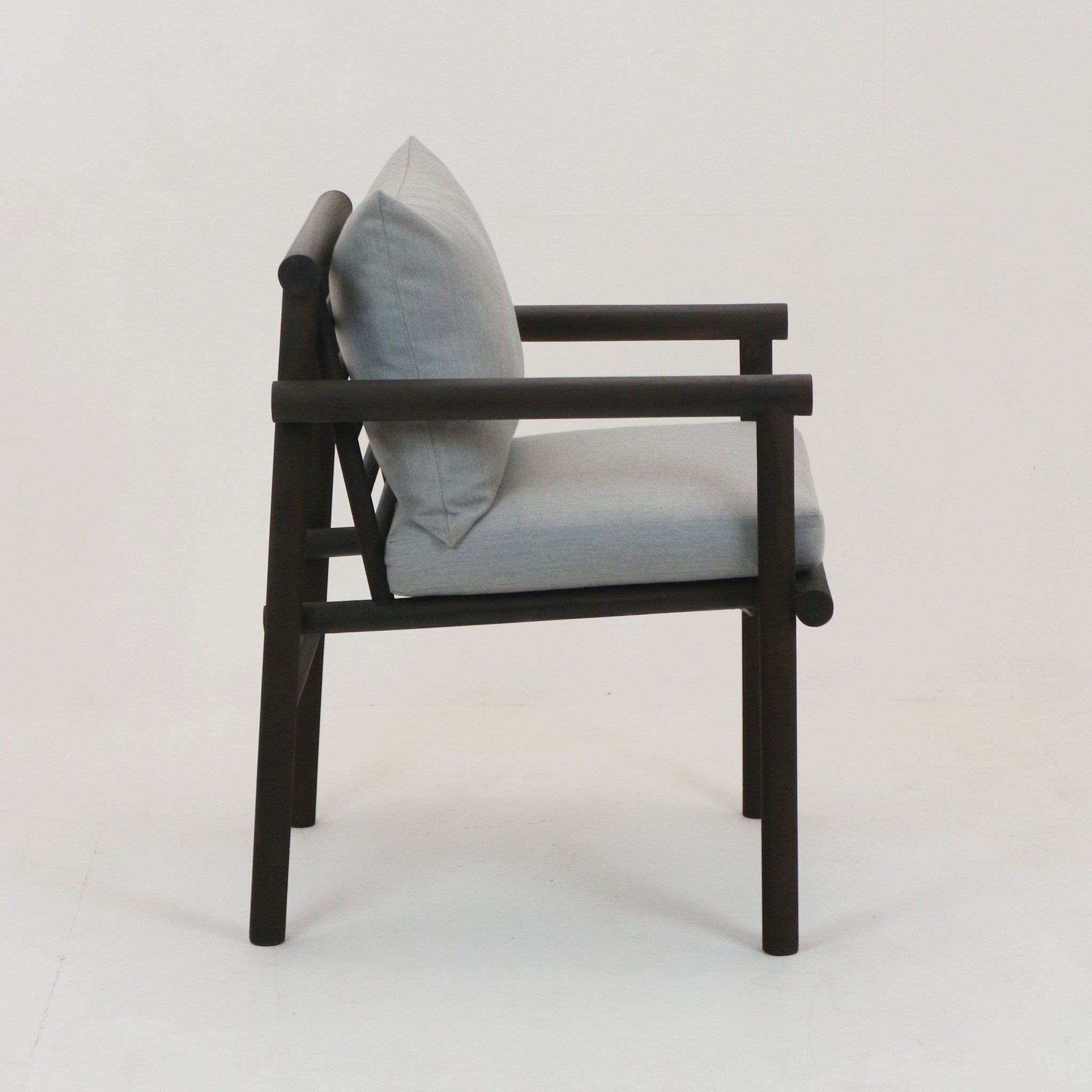 Side profile of a patio chair with a black-stained teak frame and cylindrical arm rails, fitted with light gray Sunbrella fabric seat and back cushions on a plain white background.