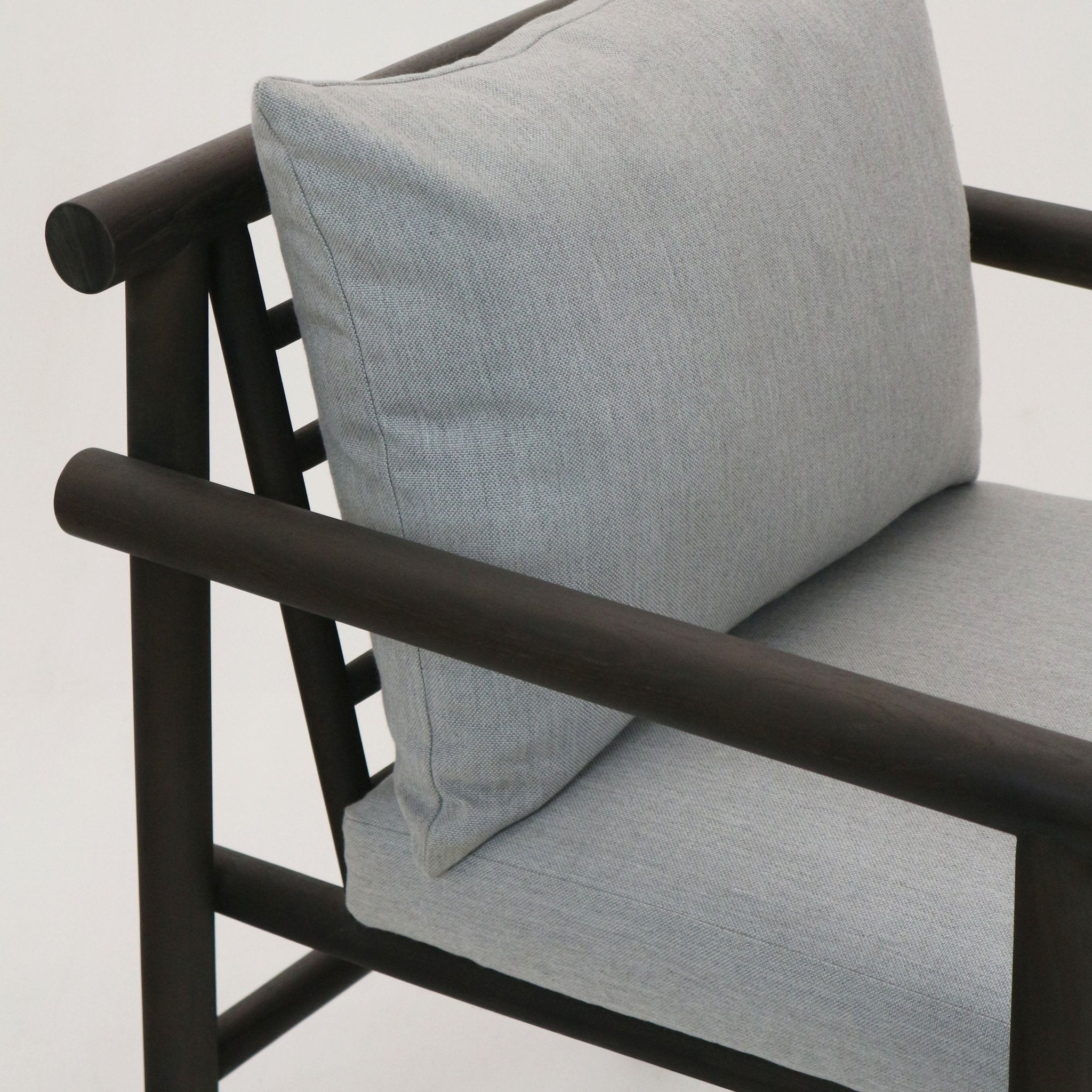 Close-up of a patio chair showing a dark teak wood frame with rounded black-stained armrests and light gray Sunbrella fabric seat and back cushions.