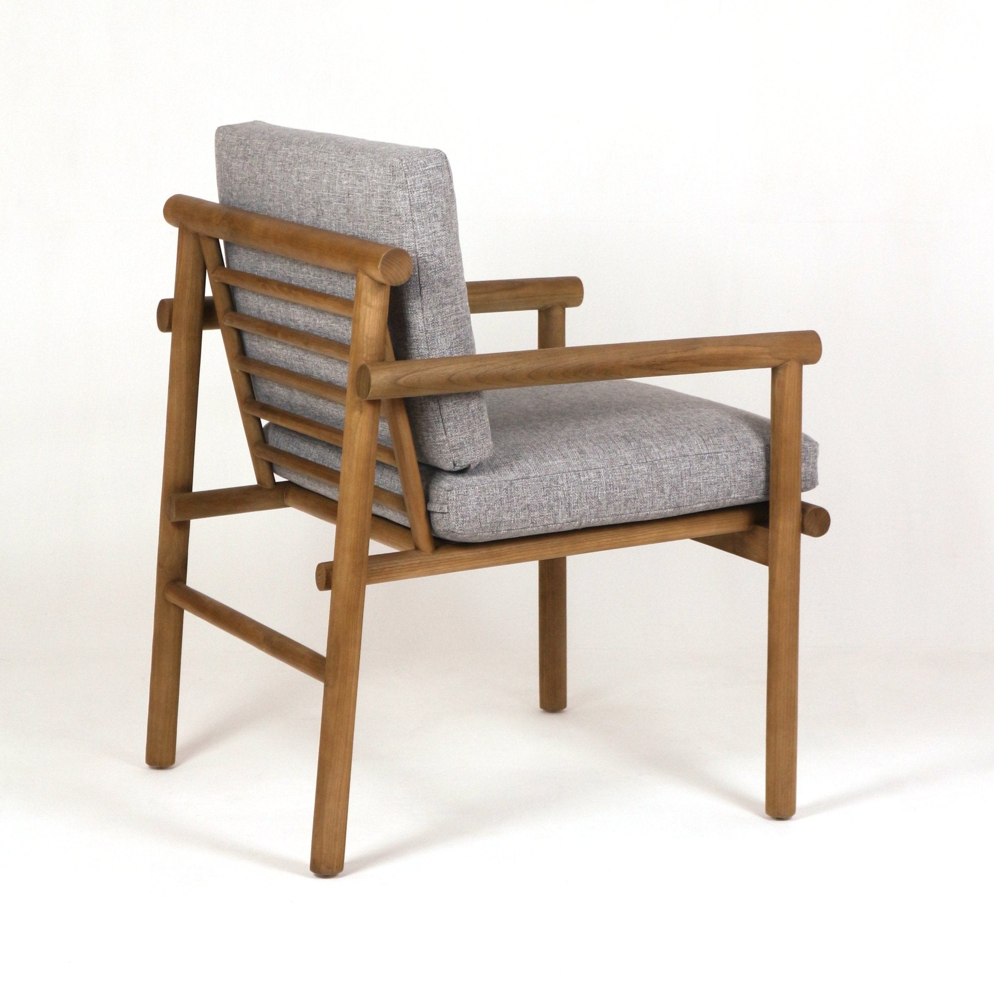 Side view of a natural teak slatted patio chair with rounded armrests and gray upholstered cushions in weather-resistant outdoor fabric.