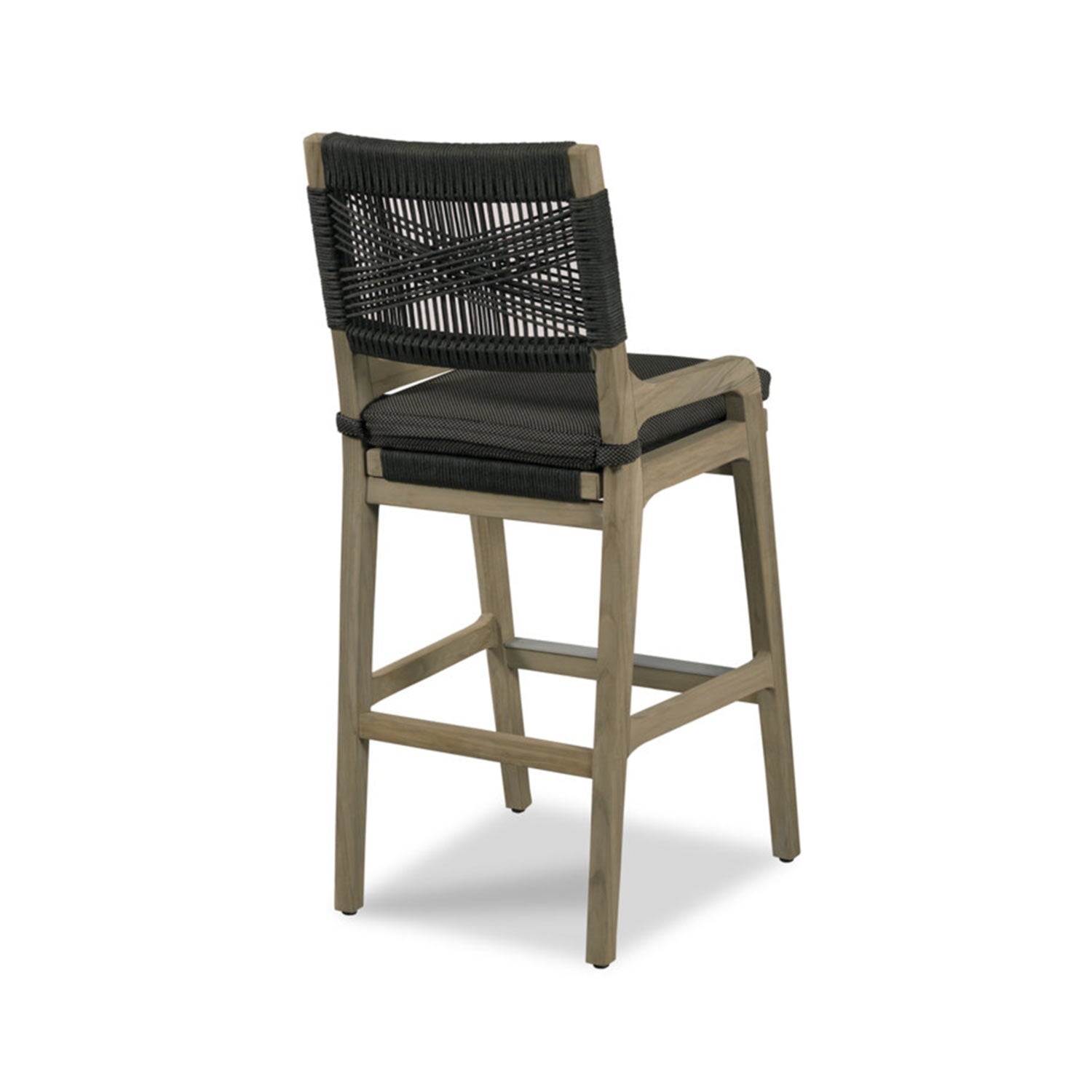 Three-quarter rear view of a natural teak outdoor bar stool featuring a black woven rope back with a crisscross pattern, black fabric seat cushion and integrated footrest for counter-height seating.