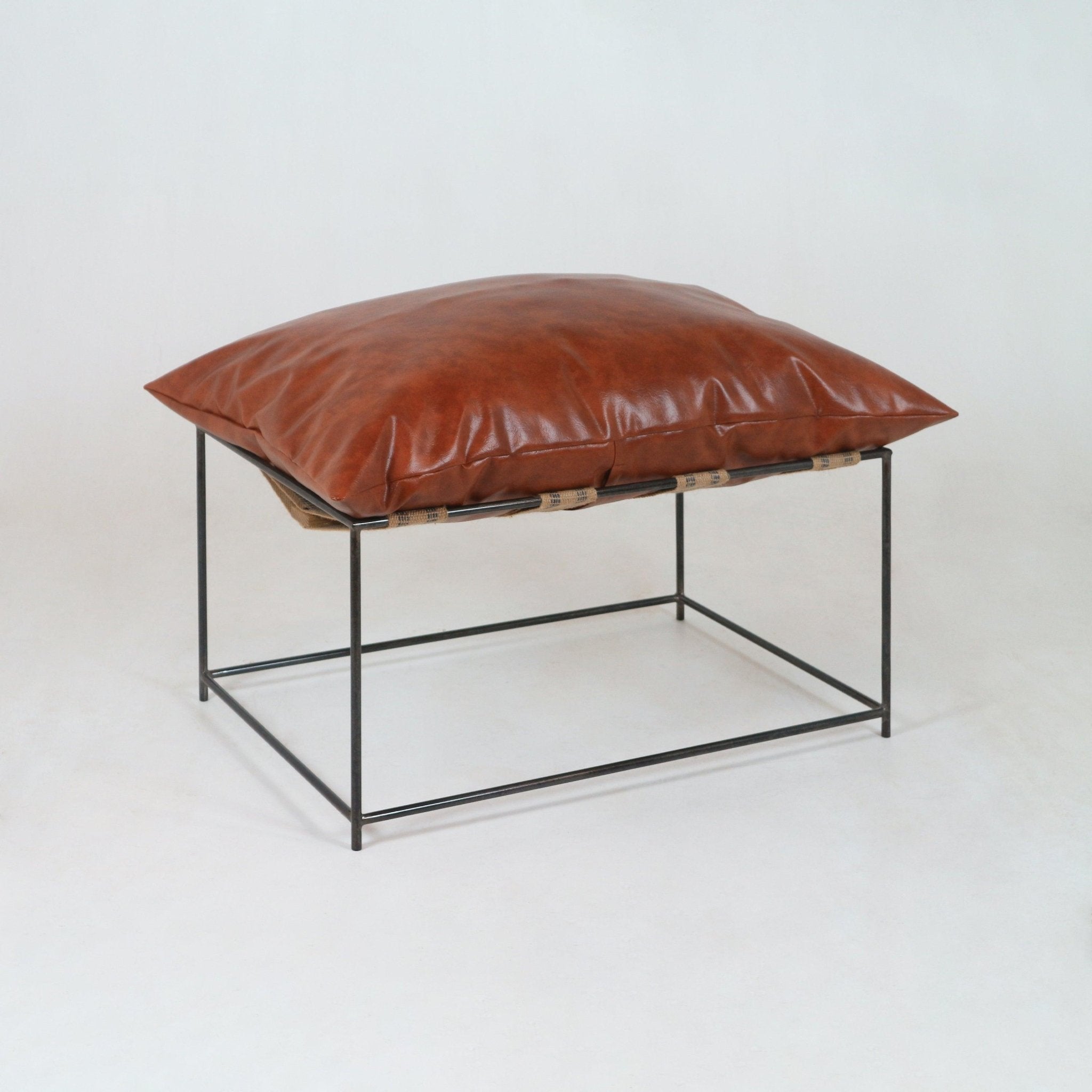 Modern pavilion ottoman with a plump red leather cushion resting on natural woven straps atop a minimalist black metal frame.