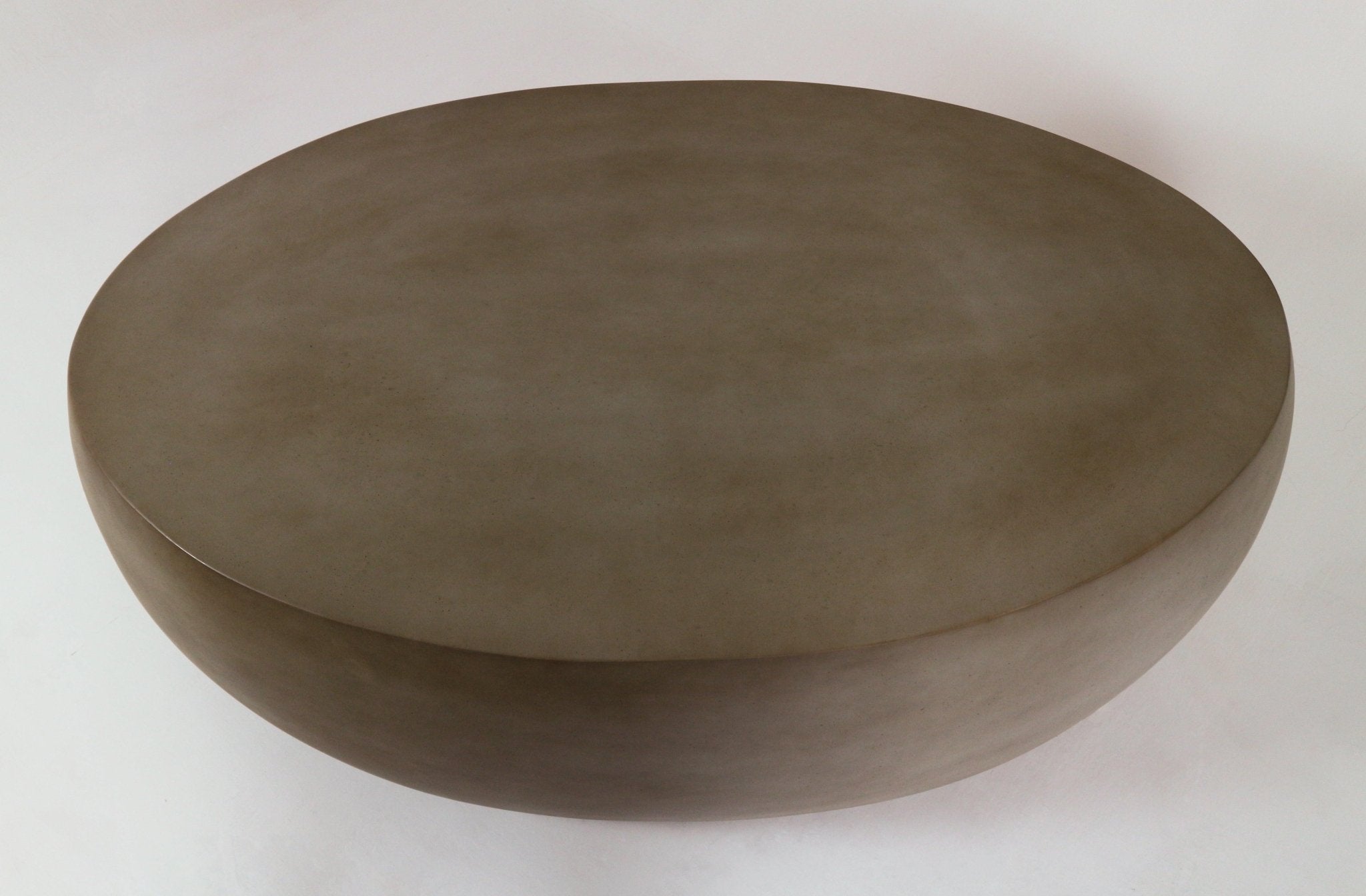 Top-down view of a modern pebble-shaped outdoor coffee table in mahogany-toned fiber concrete, showing a smooth rounded profile and subtly mottled matte surface.