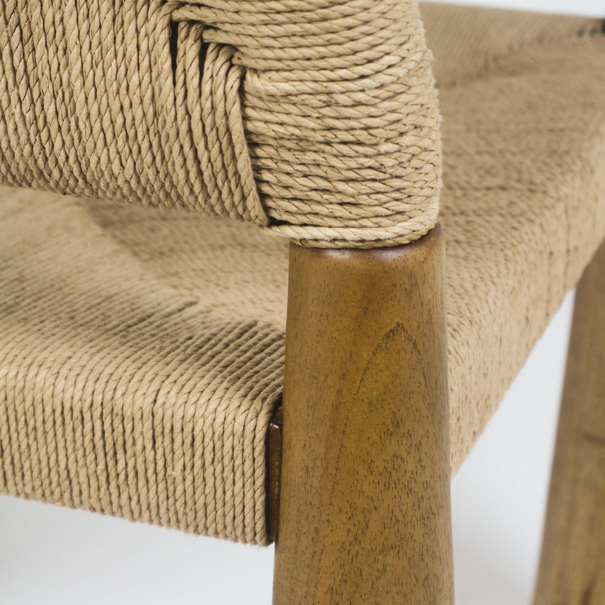 Close-up of a natural seagrass woven seat and backrest wrapped around a teak wood leg, highlighting the braided rope texture and warm natural wood grain.