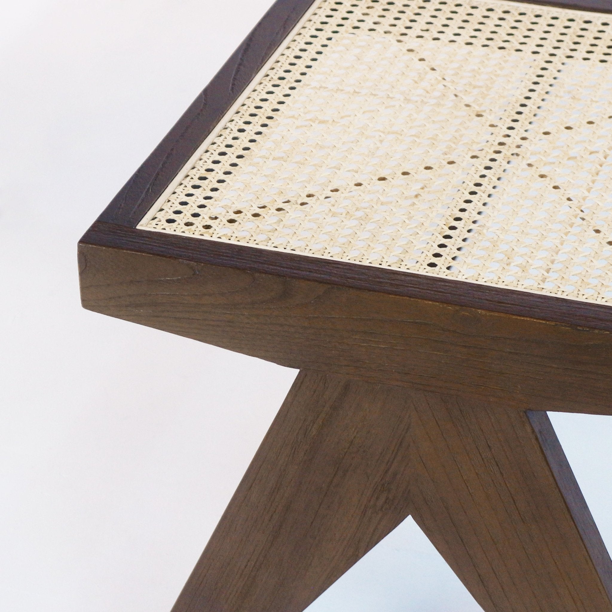Close-up of a natural cane-woven bench seat set into a dark brown solid wood frame, showing the corner joint and angled cross-leg with visible wood grain.