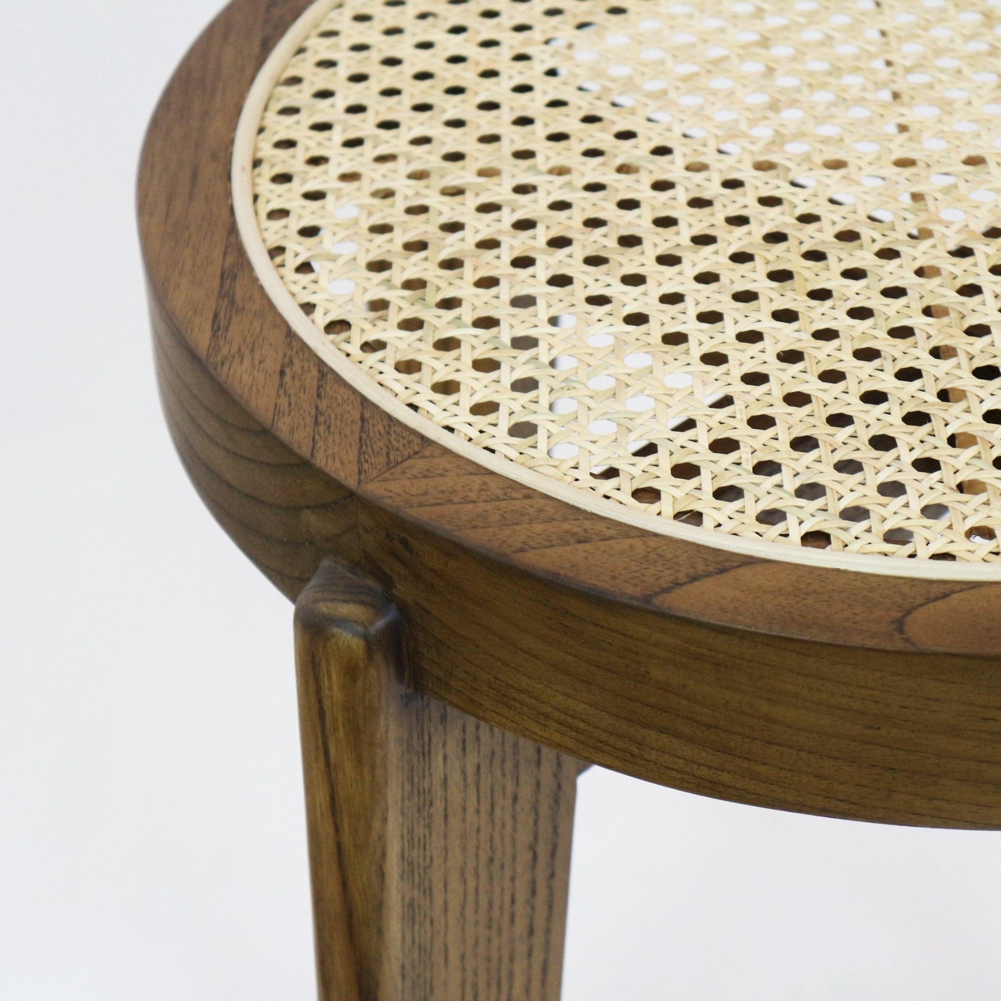 Close-up of a round counter stool showing natural rattan cane weave set into a medium brown solid wood frame and tapered leg.