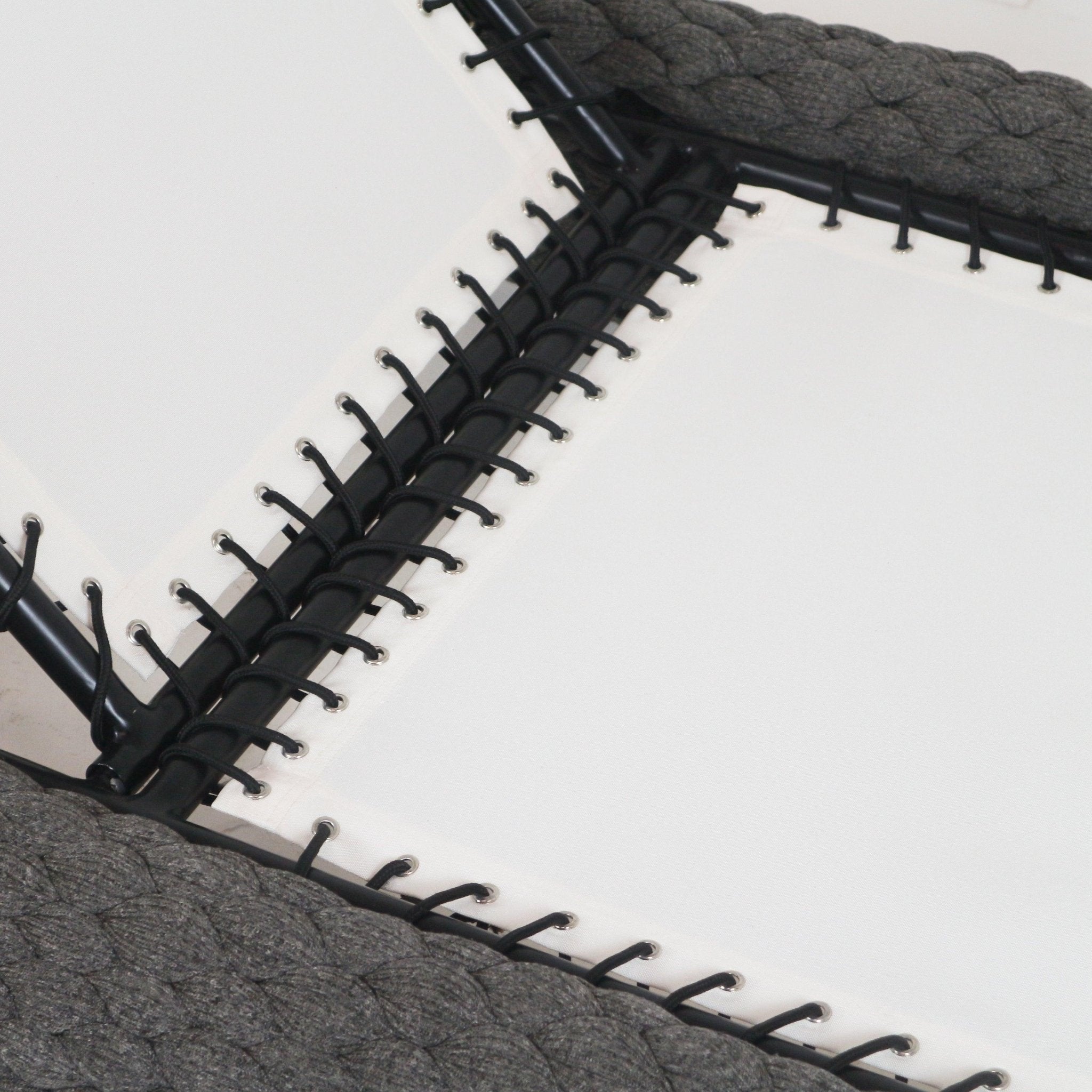 Close-up of a coastal taupe rope-woven chaise lounger edge showing black metal frame and black cord lacing threaded through silver grommets into white outdoor fabric cushion.