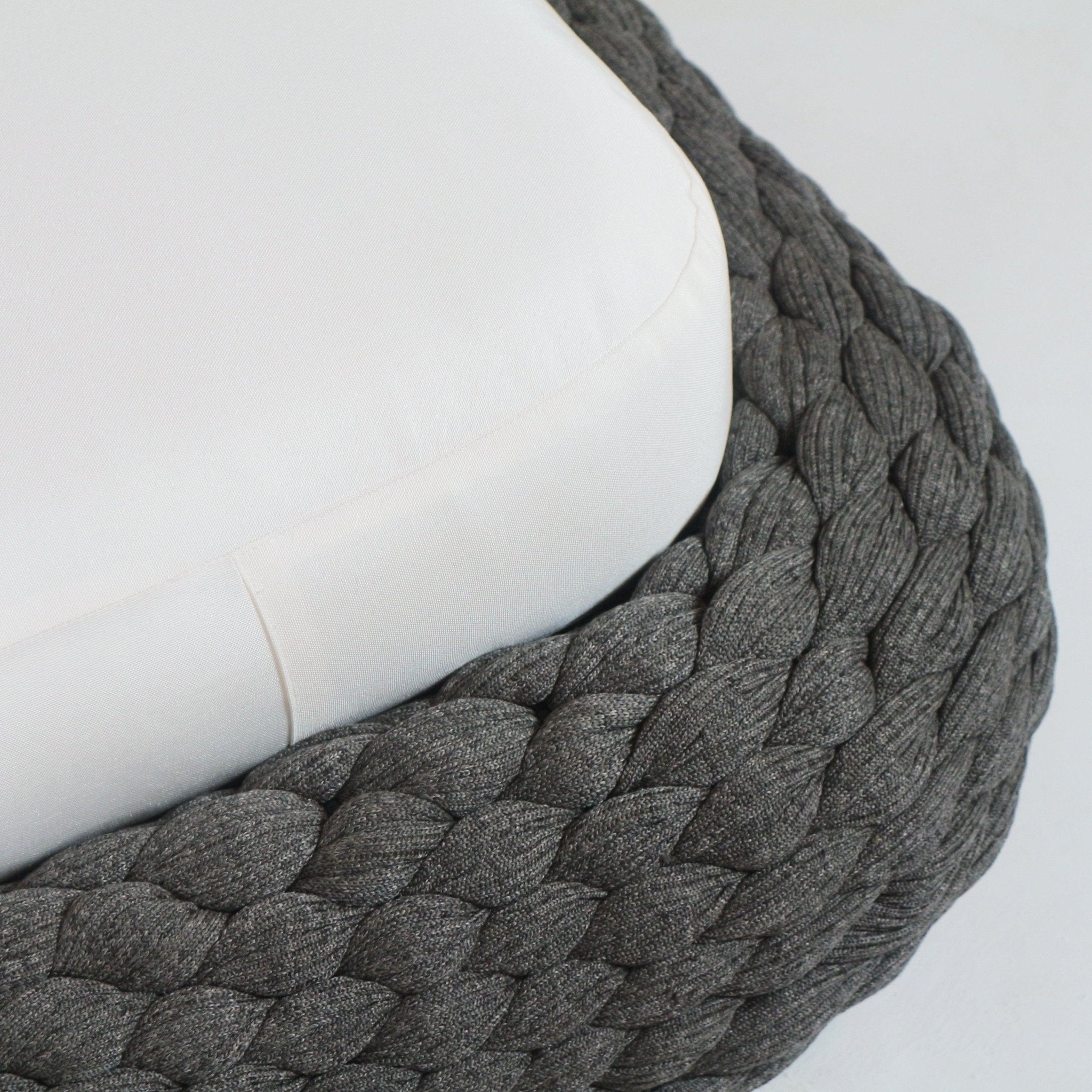 Close-up of a taupe rope-woven chaise base showing tightly braided rope texture and the rounded edge of a cream outdoor fabric seat cushion.