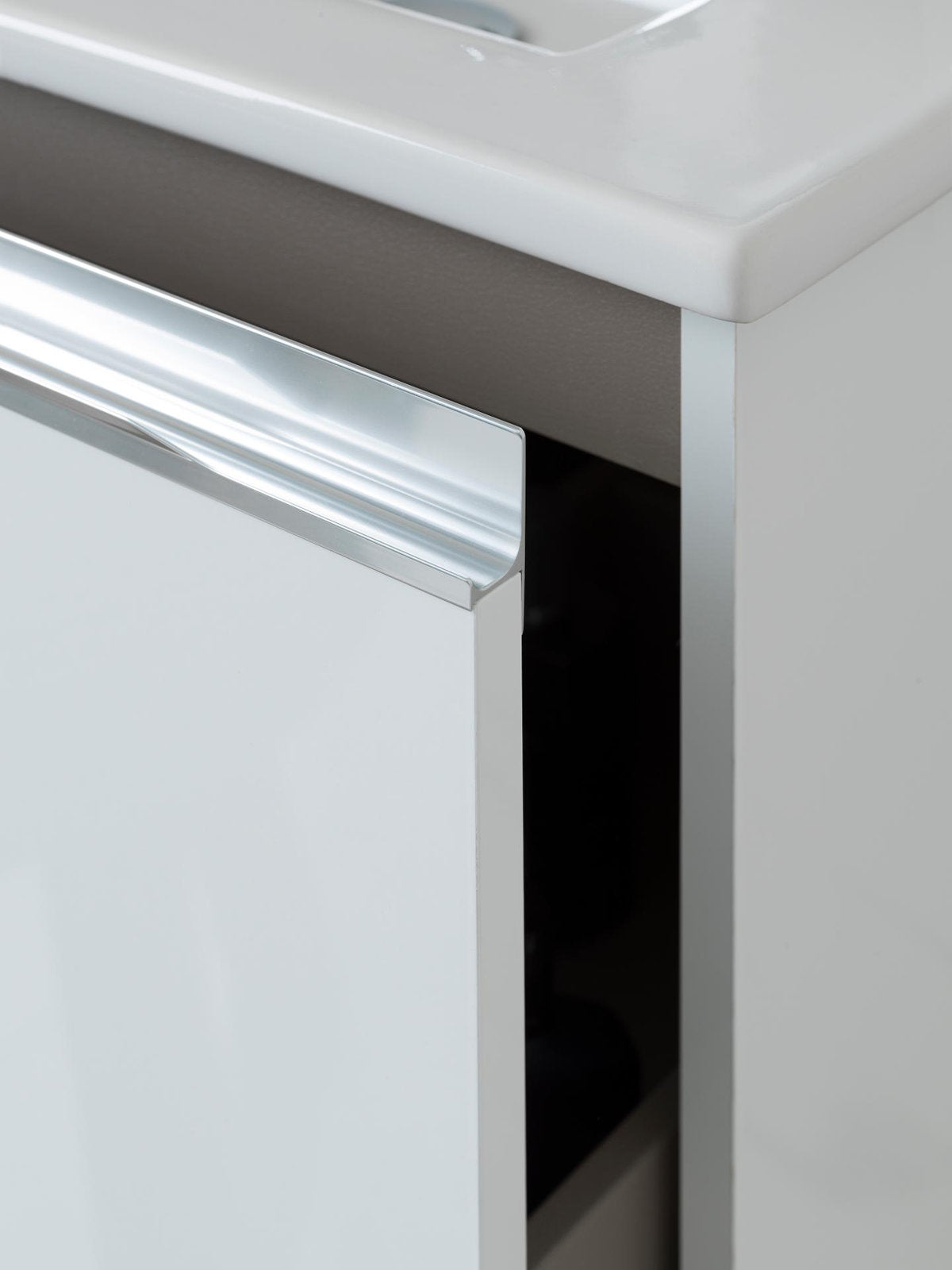 Close-up of a contemporary single-sink vanity corner showing the stone top and ceramic sink edge, a glossy stone-colored drawer front with integrated chrome handle and a partially open storage drawer on the solid wood cabinet.