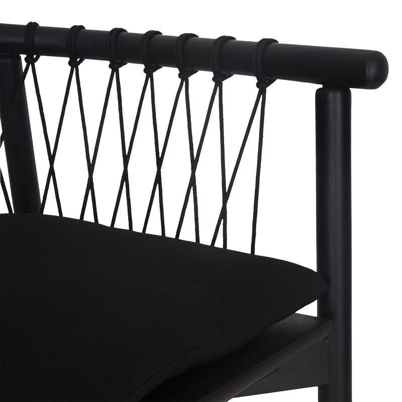 Close-up of a modern black dining chair showing a solid wood frame with a rounded top rail, woven black rope X-pattern backrest and a black upholstered fabric seat cushion.