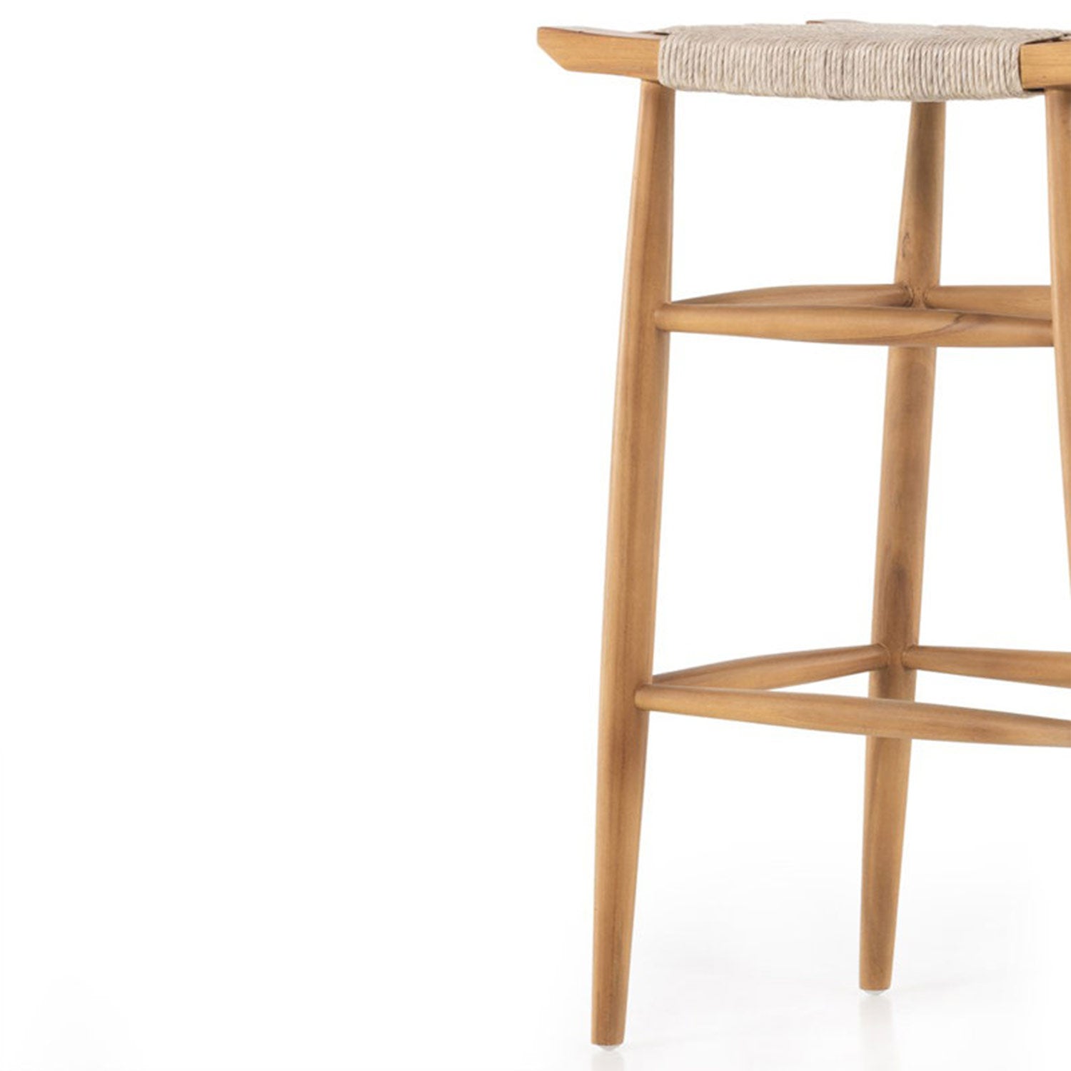 Close-up of the right side of a backless natural teak outdoor bar stool showing tapered legs, rounded footrest rails and a woven natural-fiber seat edge in a coastal Scandinavian style.