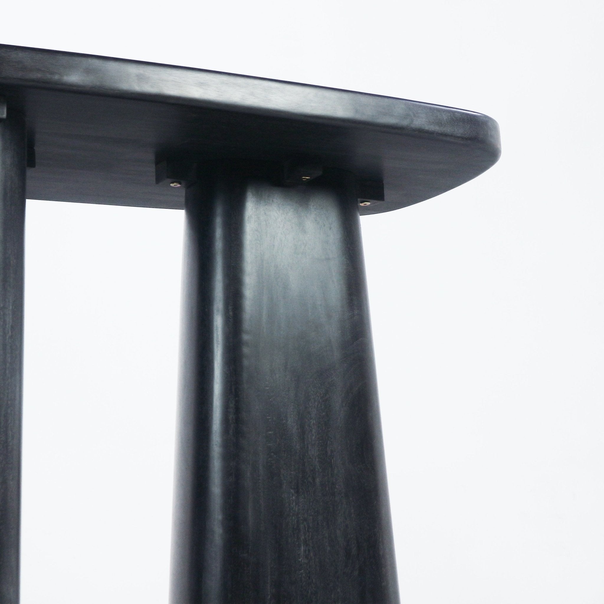 Close-up of a black solid wood console showing the tapered leg and underside of the tabletop with a smooth rounded edge, subtle wood grain and small visible metal fasteners.