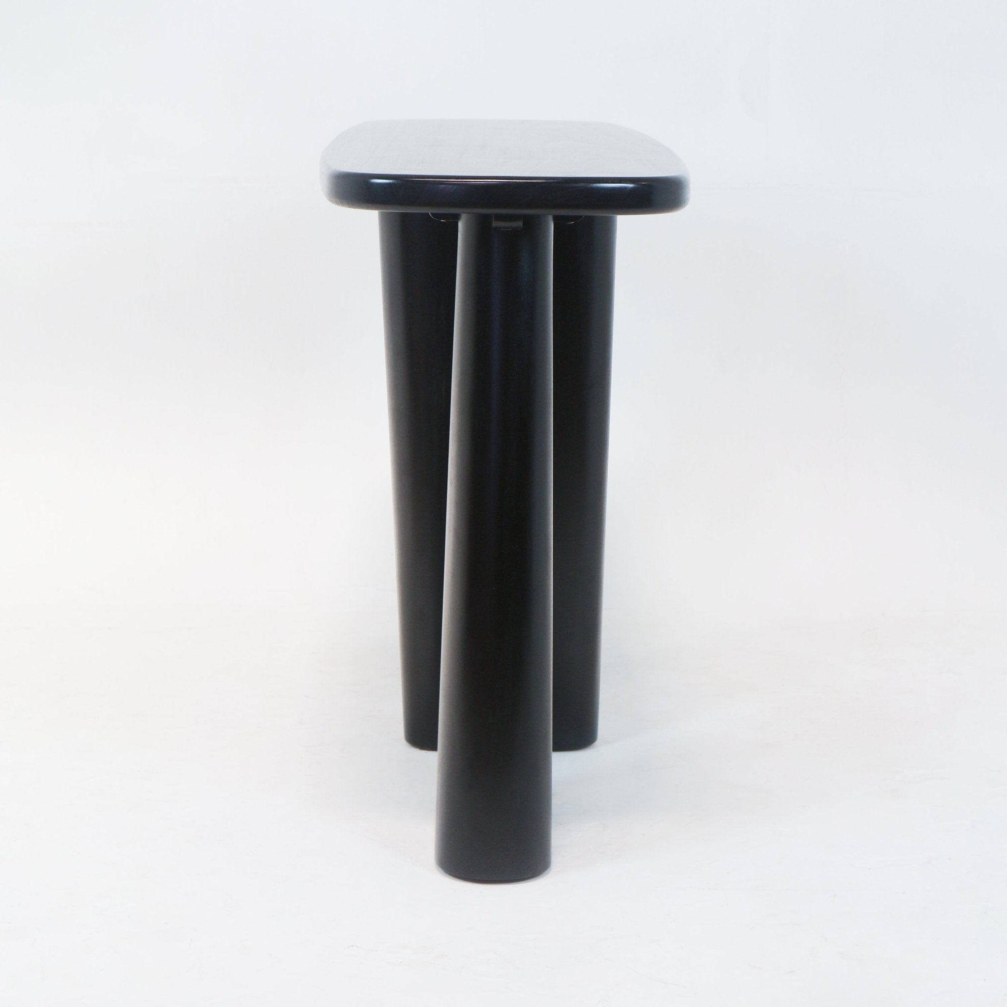 Front view of a modern solid wood console in smoked black showing a rounded rectangular top and three thick cylindrical legs against a white studio background.