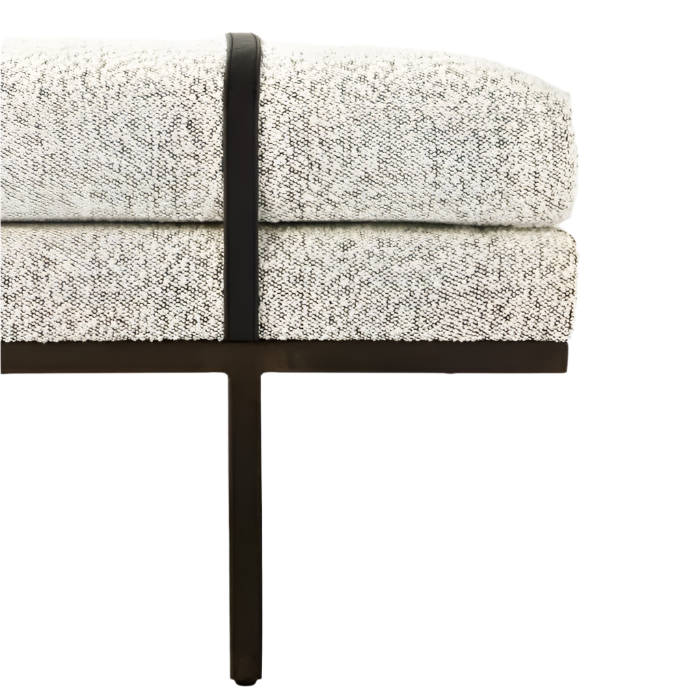 Close-up of an end-of-bed bench corner showing textured natural-colored boucle fabric cushions, a dark metal T-style leg and a vertical black strap accent.