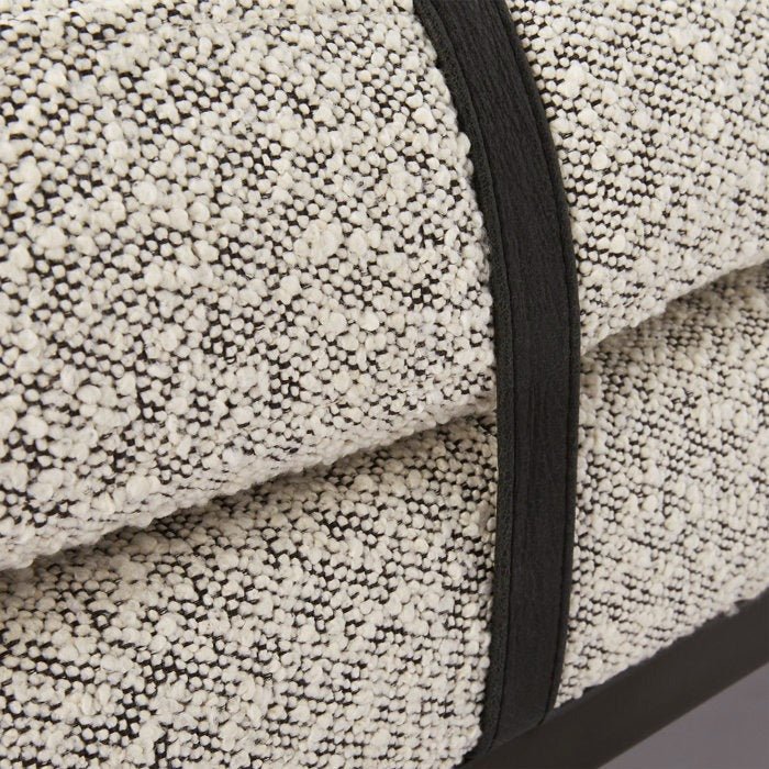 Close-up of natural cream boucle fabric on an end-of-bed bench, showing looped texture, a contrasting dark fabric strap and a glimpse of the natural wood base.