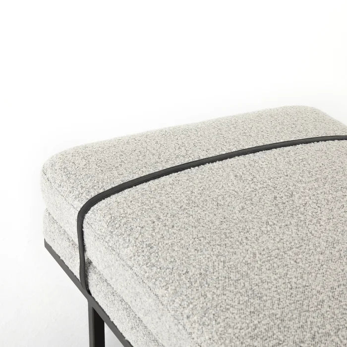 Close-up of a natural-colored boucle fabric bench seat with contrasting dark piping and a slim dark frame, styled as a coastal-modern end-of-bed bench.
