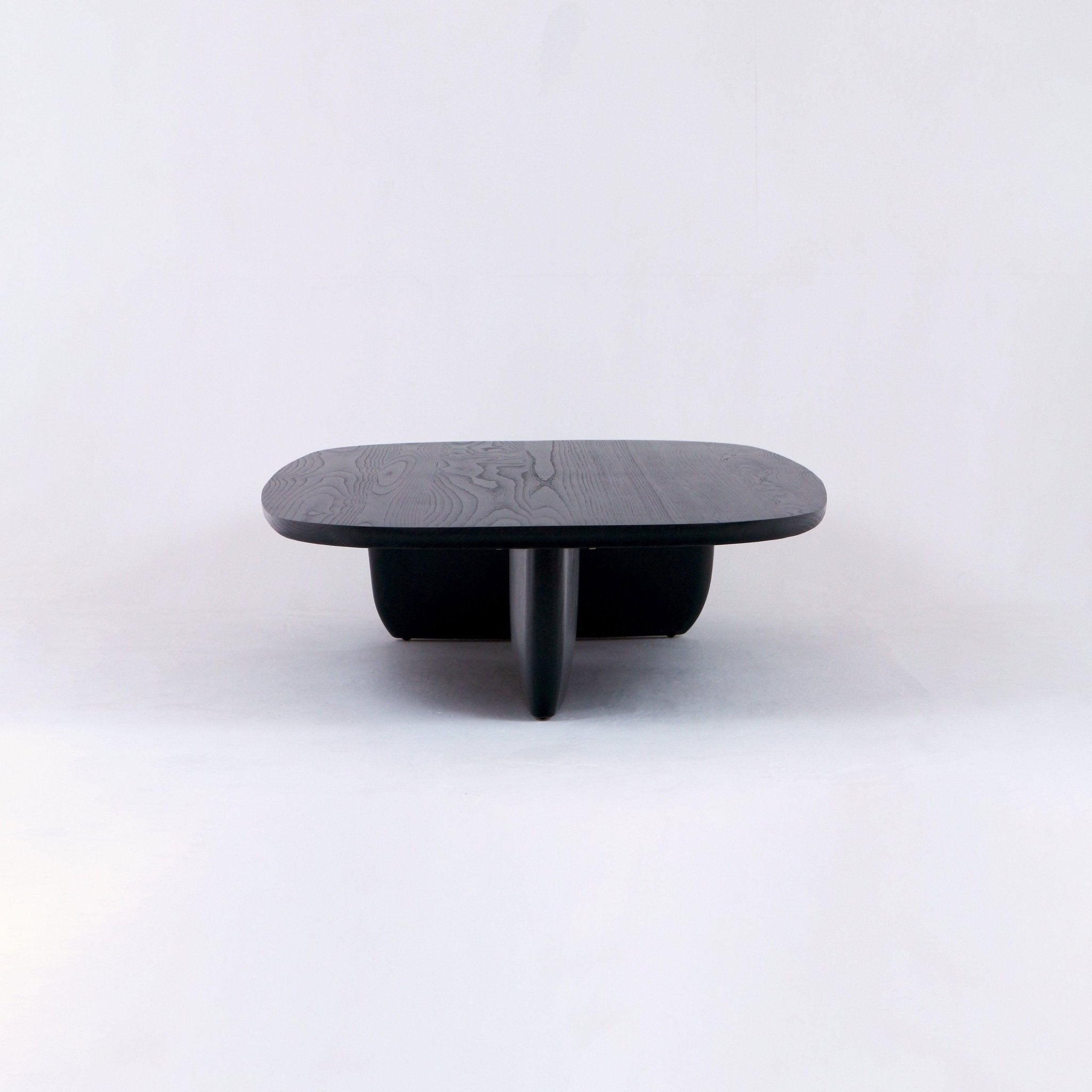 Low modern coffee table in black oak with a rounded rectangular wood-grain top and sculptural central pedestal base, shown on a clean white background.