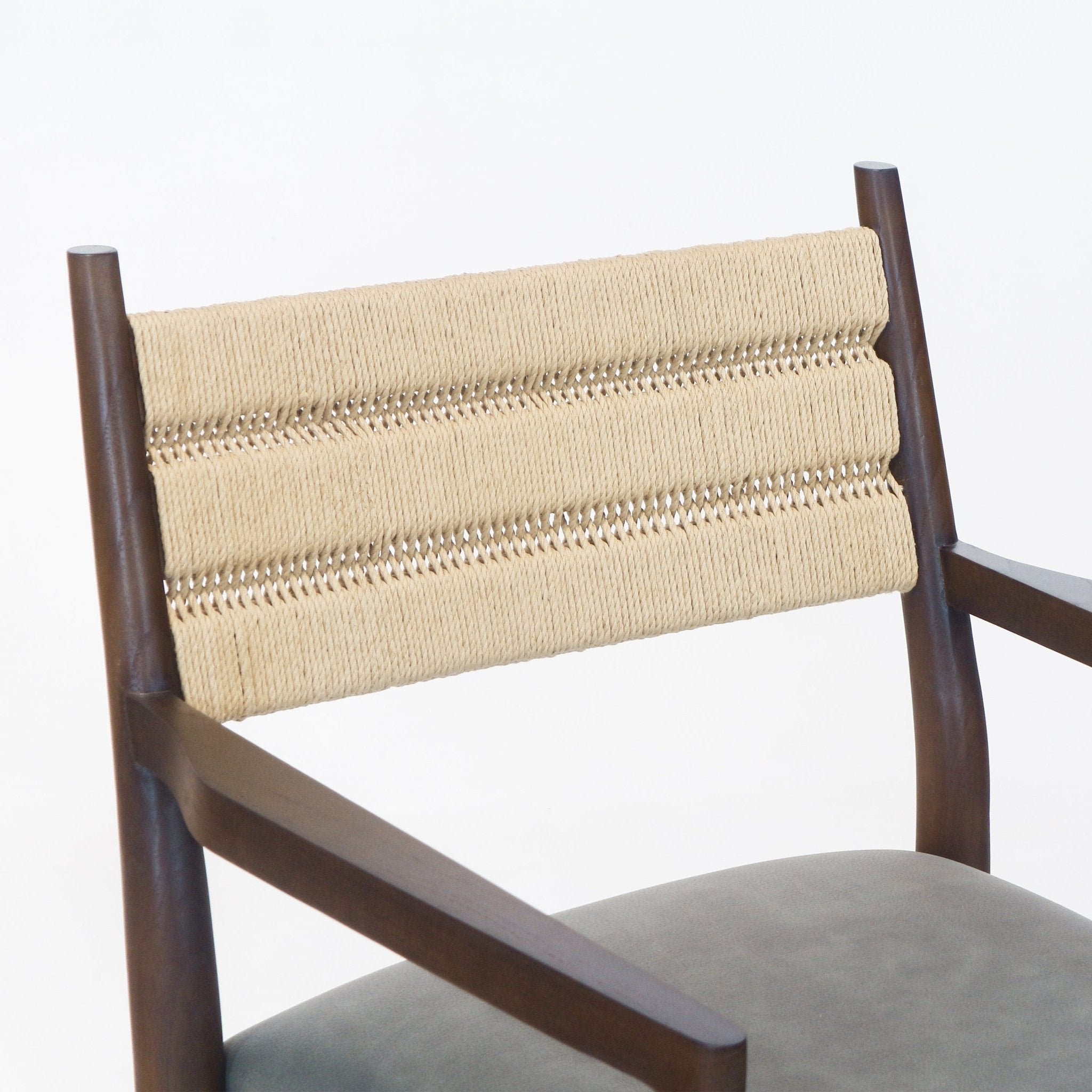 Close-up of a dining chair showing a natural woven rope backrest stretched between dark stained solid wood arm posts, angled wooden arms and a tan leather seat cushion.