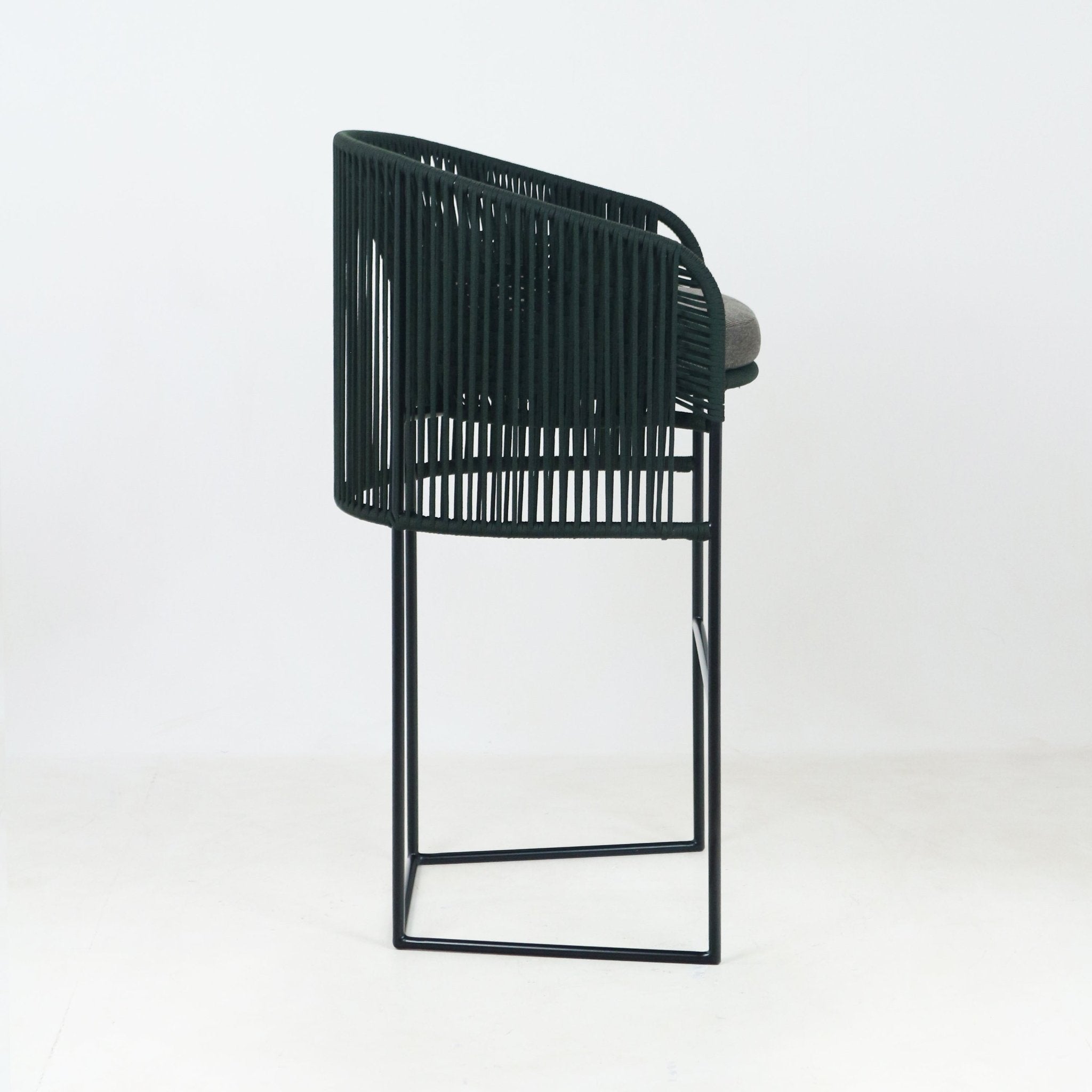 Side view of an outdoor counter stool with a dark green woven rope backrest, gray fabric seat cushion, and slender black metal sled-style base.
