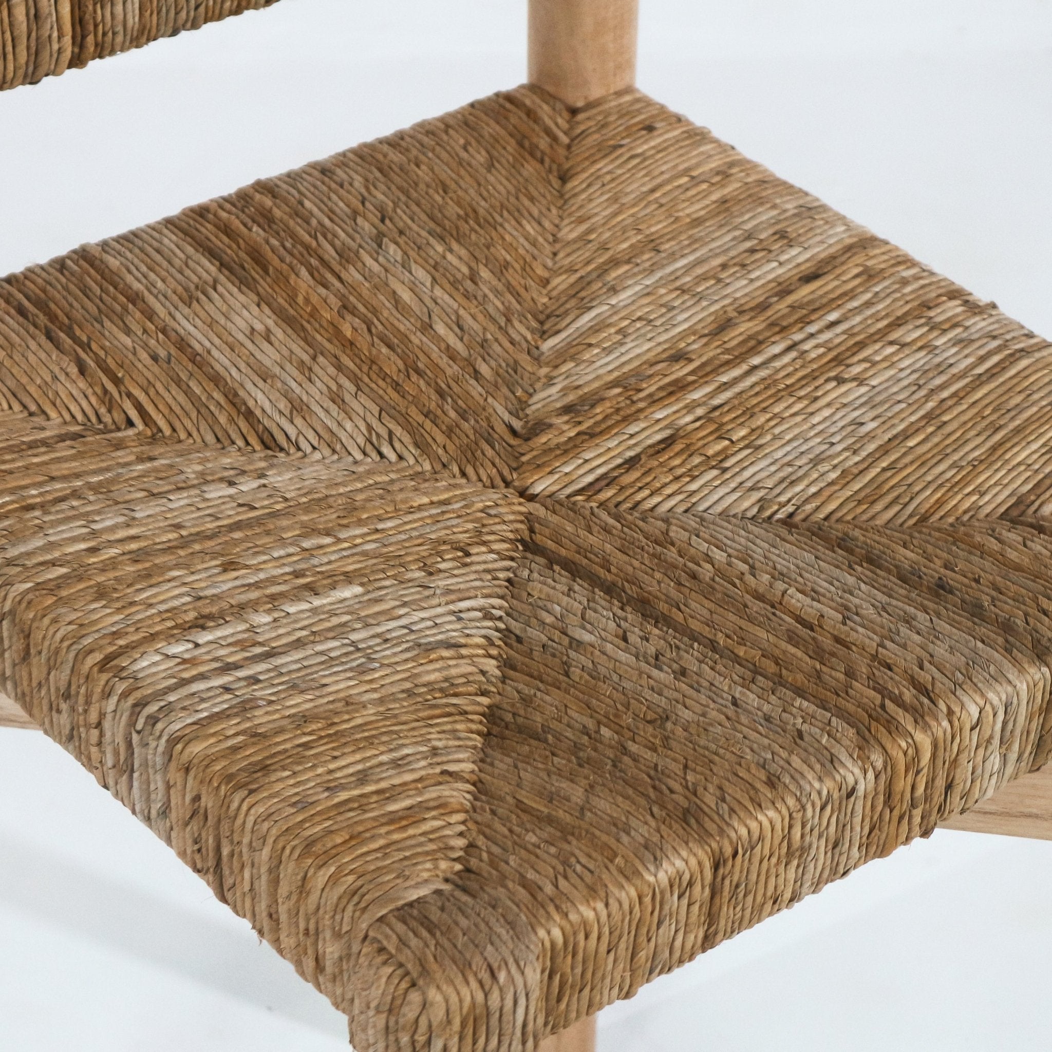 Close-up of a natural seagrass woven counter stool seat showing a four-panel chevron weave and rounded edge, with a light teak wood leg visible in warm natural tones for a coastal look.