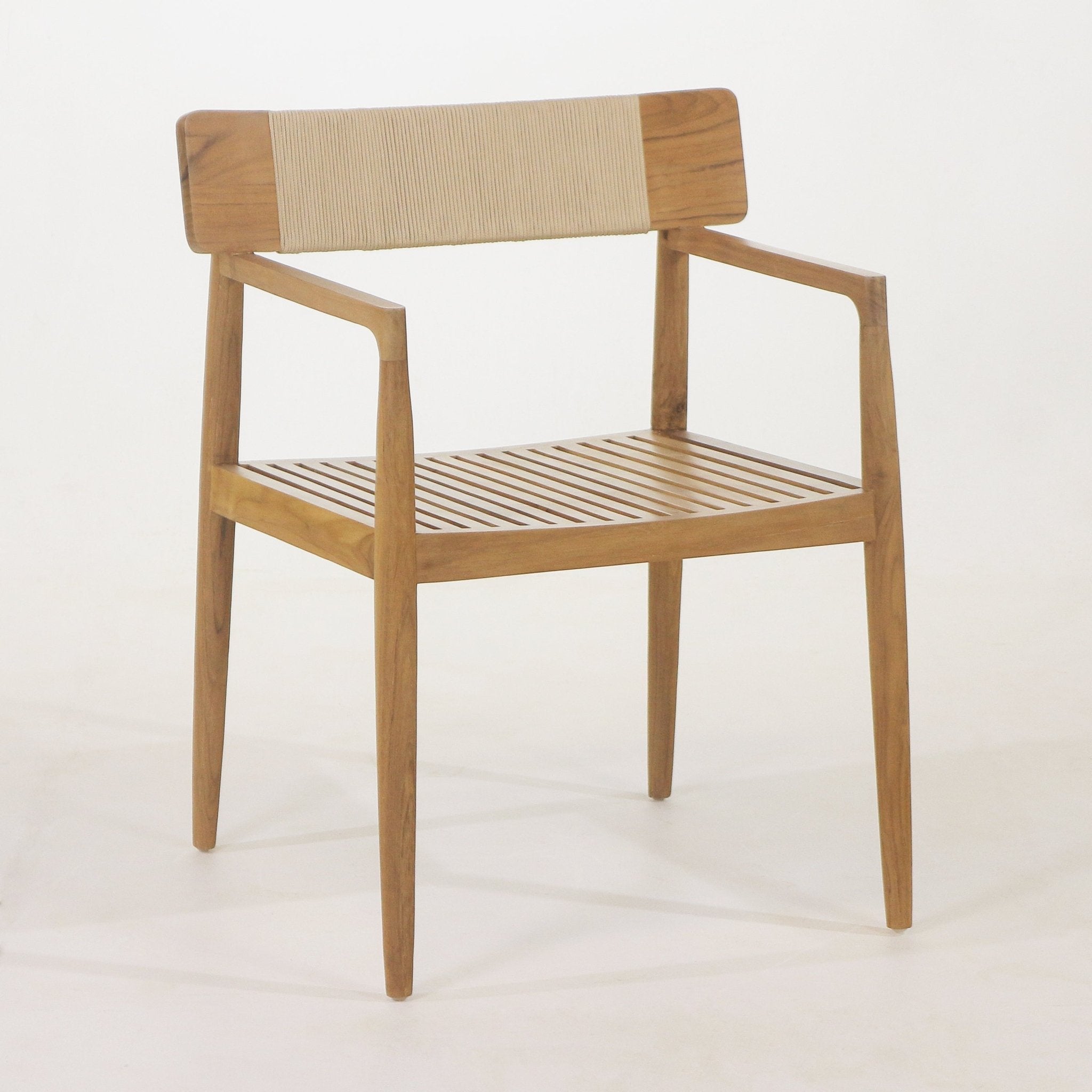 Natural teak outdoor dining chair with a slatted wood seat, tapered legs, angular armrests and a beige woven back panel in a mid-century modern coastal style.