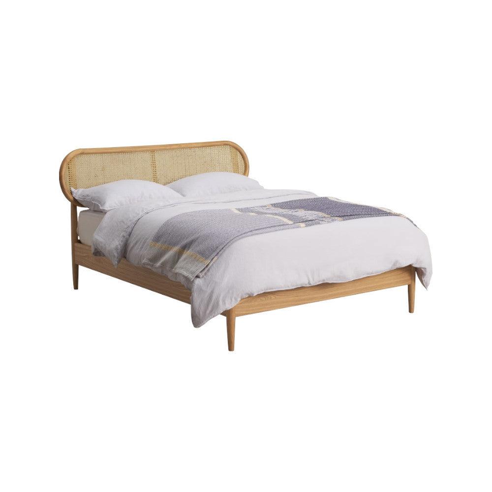 King-size modern platform bed in natural solid wood with a rounded cane rattan headboard and tapered legs, shown dressed with white linens and a gray-blue throw.