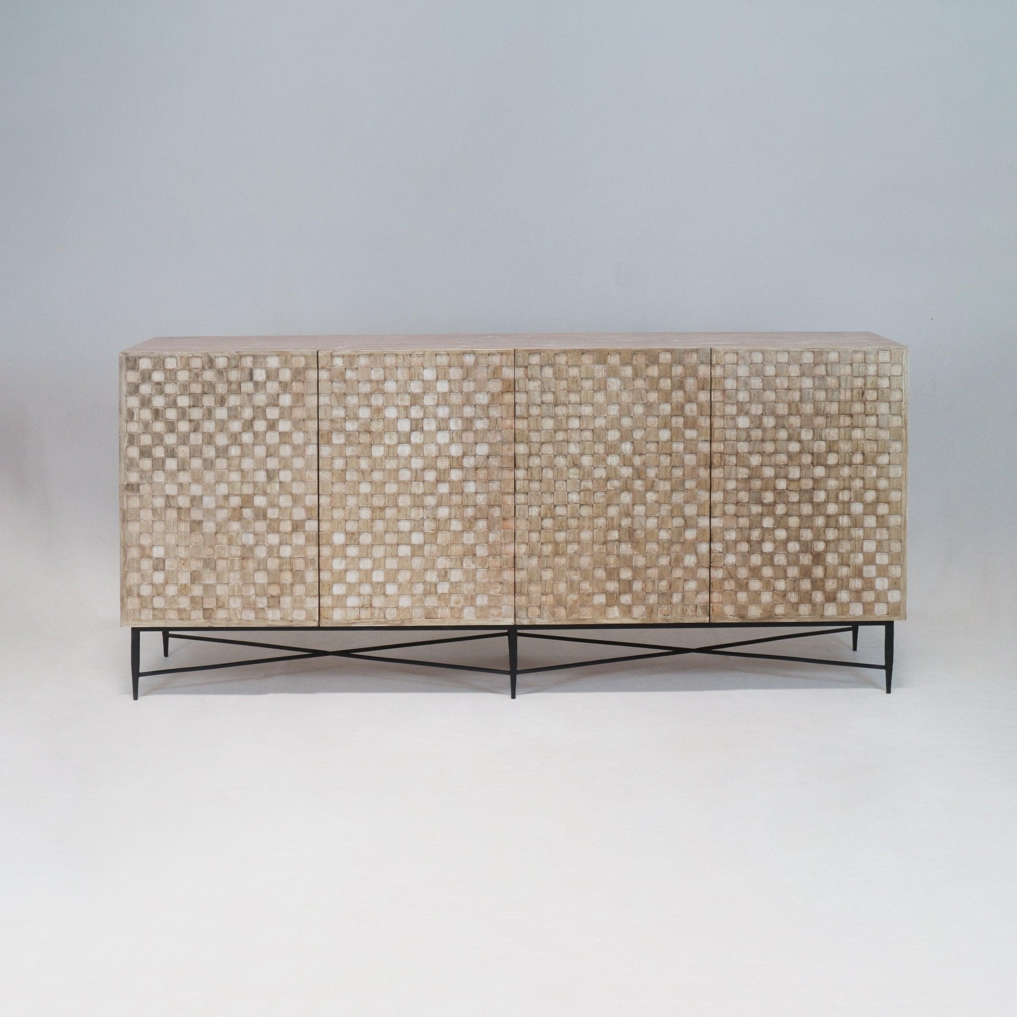 Long teak sideboard with textured checkerboard front panels in a natural finish, four doors and a slim black metal base with crisscross stretcher, photographed against a neutral studio background.