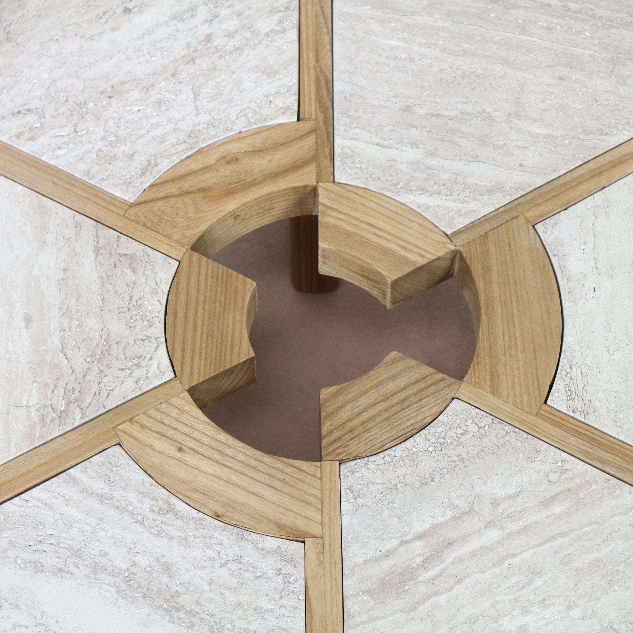 Close-up of a travertine coffee table top with natural oak inlay: light beige travertine panels divided by oak spokes forming a circular recessed center with four notched oak supports.