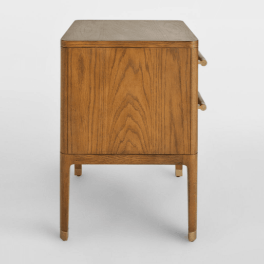Side view of a brown solid wood two-drawer nightstand showing warm wood grain, rounded brass drawer pulls and tapered legs with brass-capped feet in a contemporary glam style.
