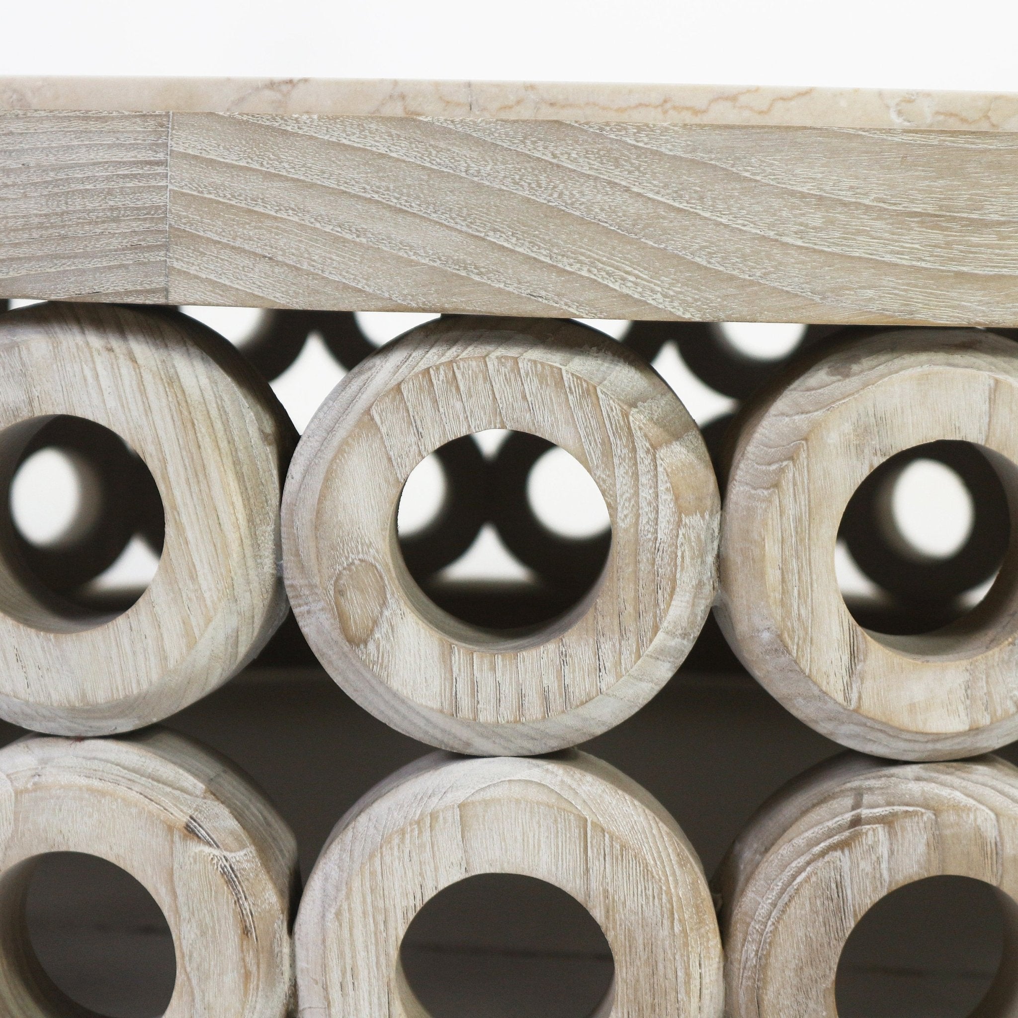 Close-up of a natural oak circular hollow base with repeating round cutouts supporting a beige travertine tabletop, showing detailed wood grain texture and carved circular openings.