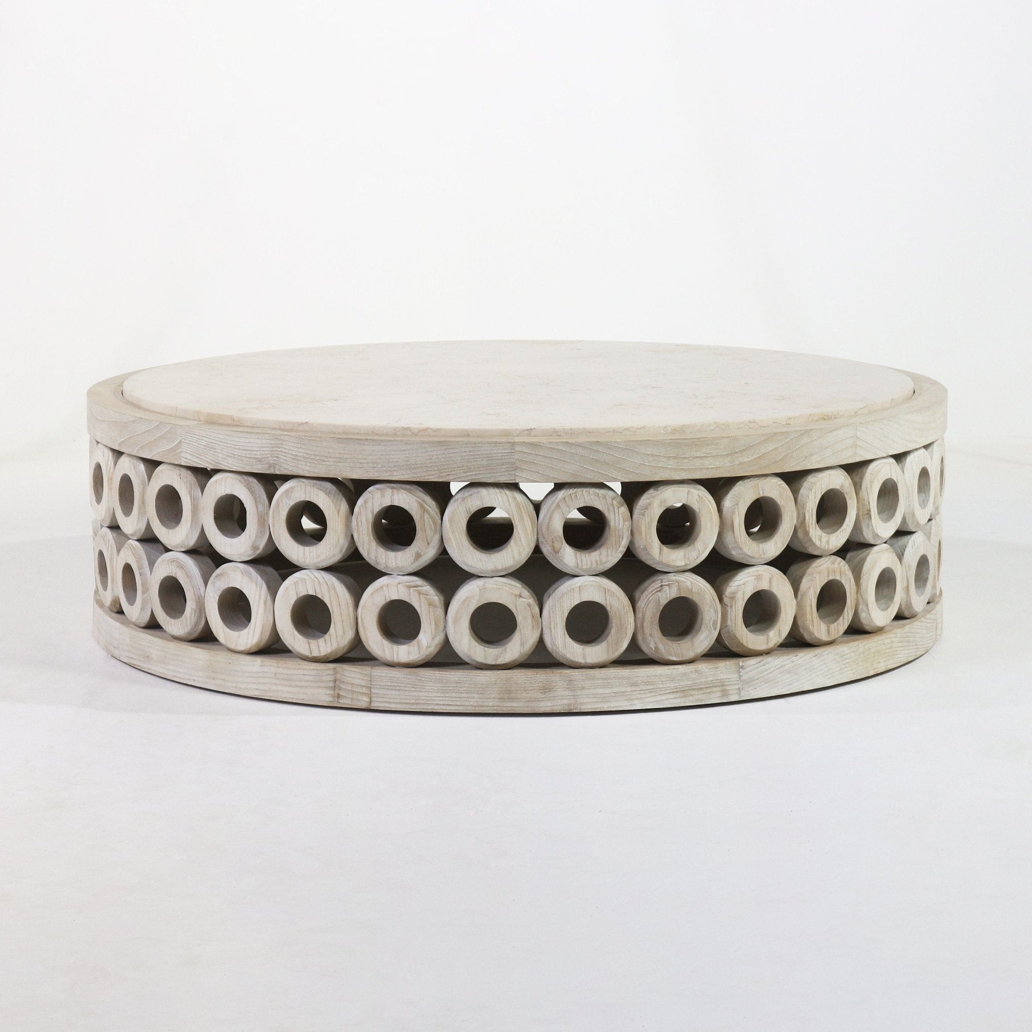 Low round coffee table with a pale travertine top and natural oak base featuring two stacked rows of carved hollow circular rings around the perimeter, in a modern contemporary style.