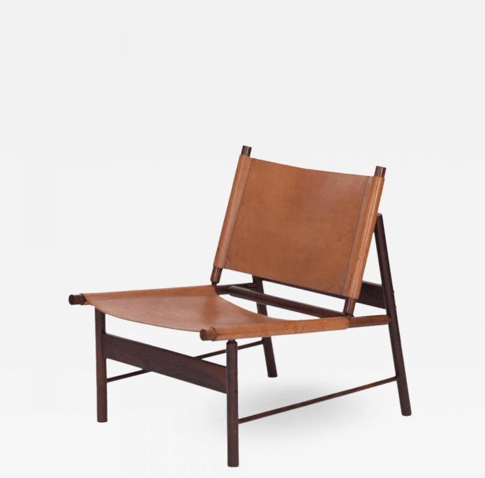 Low-profile mid-century modern lounge chair with stretched tan leather seat and back suspended on a dark teak wood frame; armless design with angled legs and visible dowel joinery.