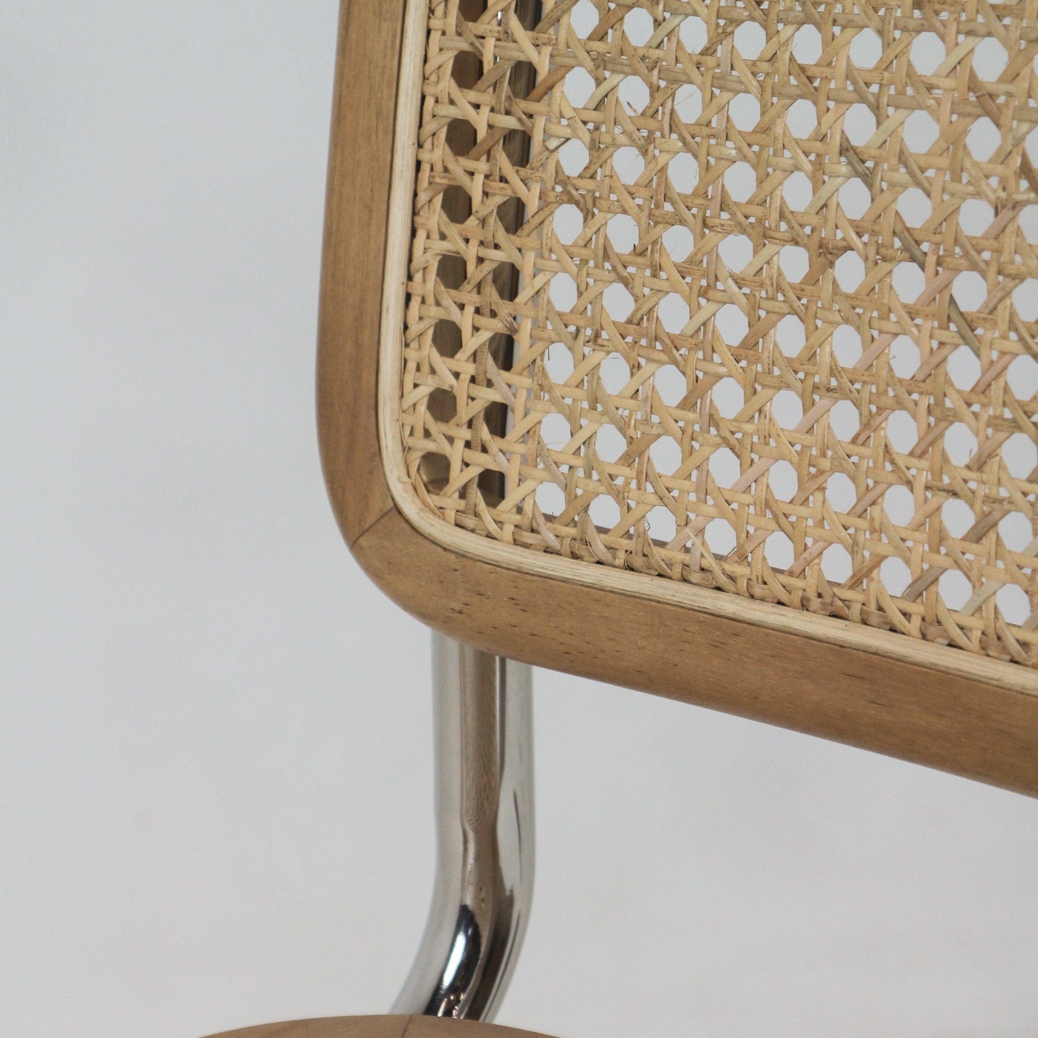 Close-up of the woven rattan cane back set in a warm teak frame with a polished aluminium tubular leg visible below, highlighting natural texture and mid-century boho styling.