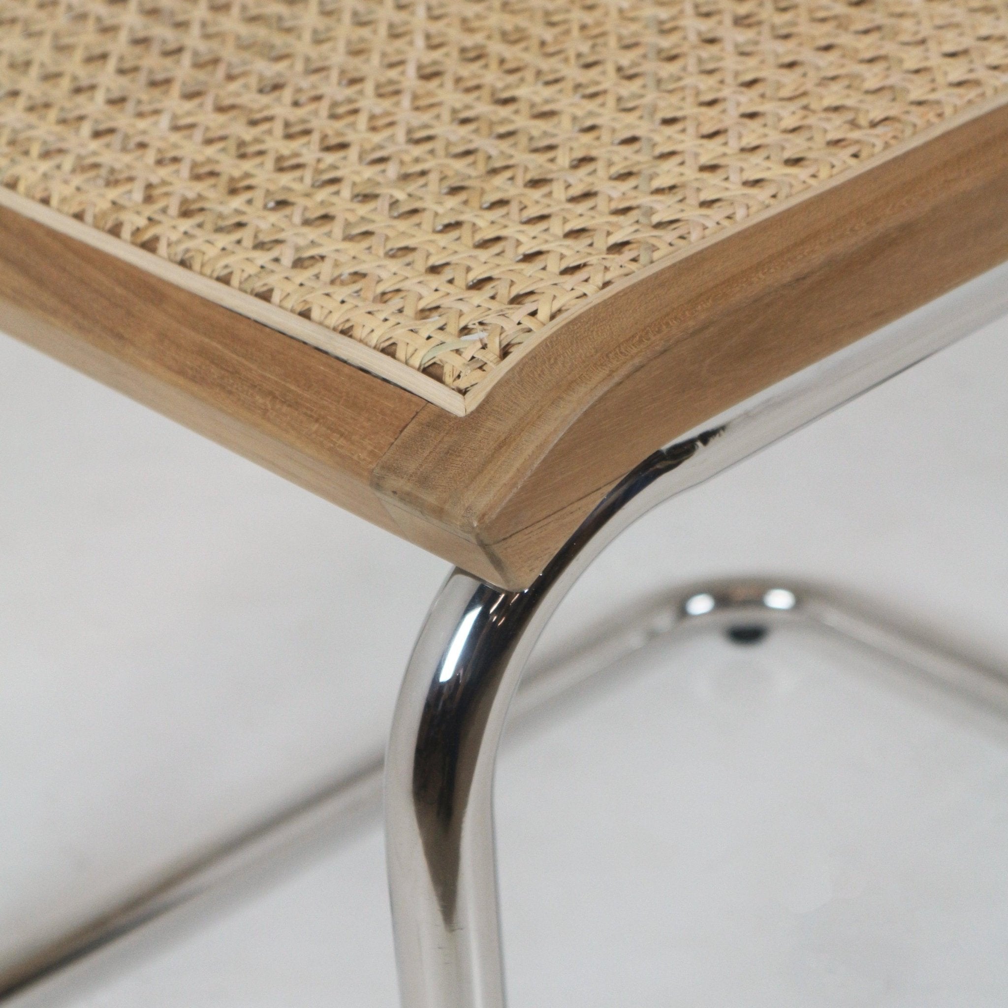 Close-up of a natural teak wood chair corner featuring woven rattan cane seat inset and a polished chrome aluminum cantilever leg.