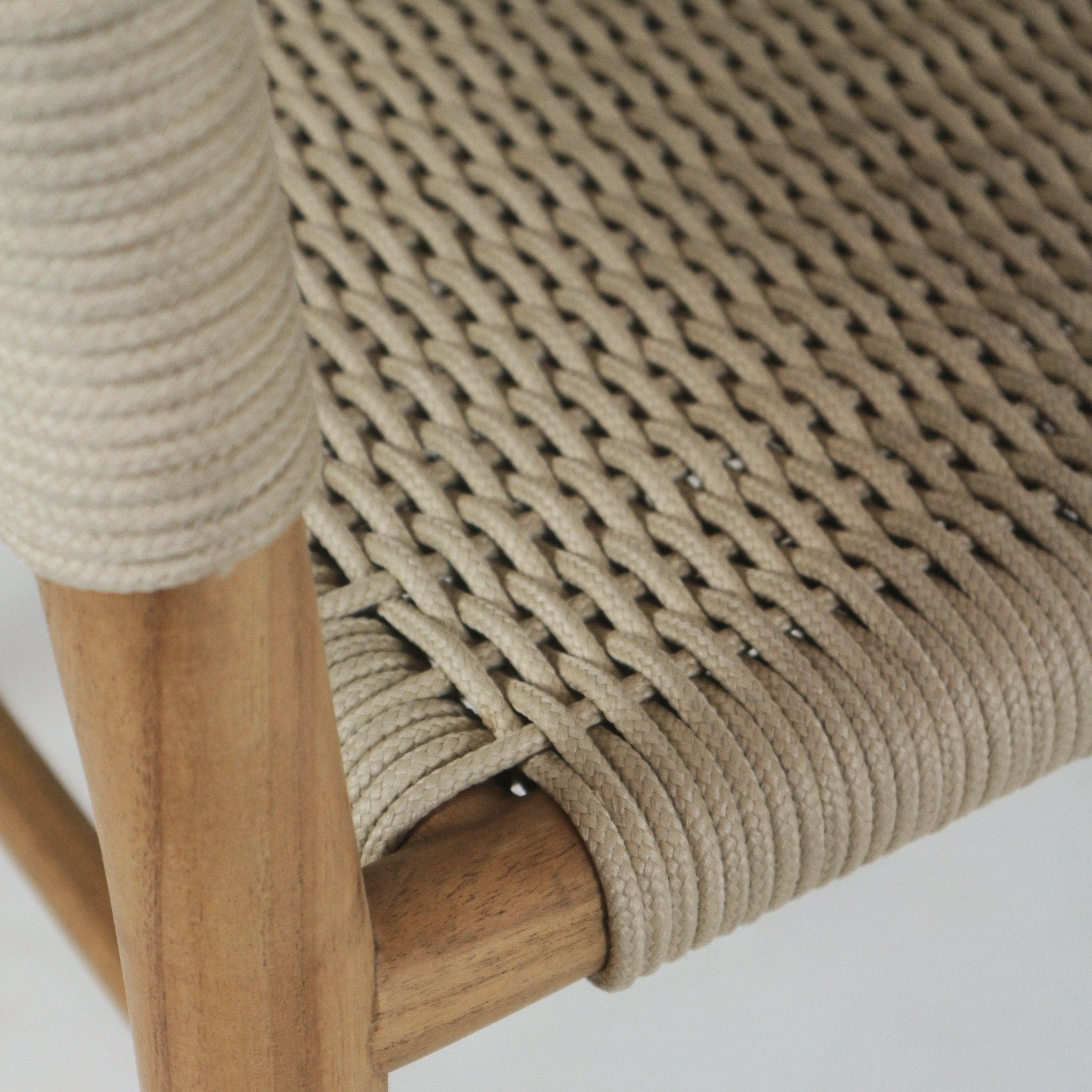Close-up of a beige polypropylene rope seat tightly woven over a natural teak wood frame, highlighting the braided seat pattern and rope-wrapped teak rail joint.
