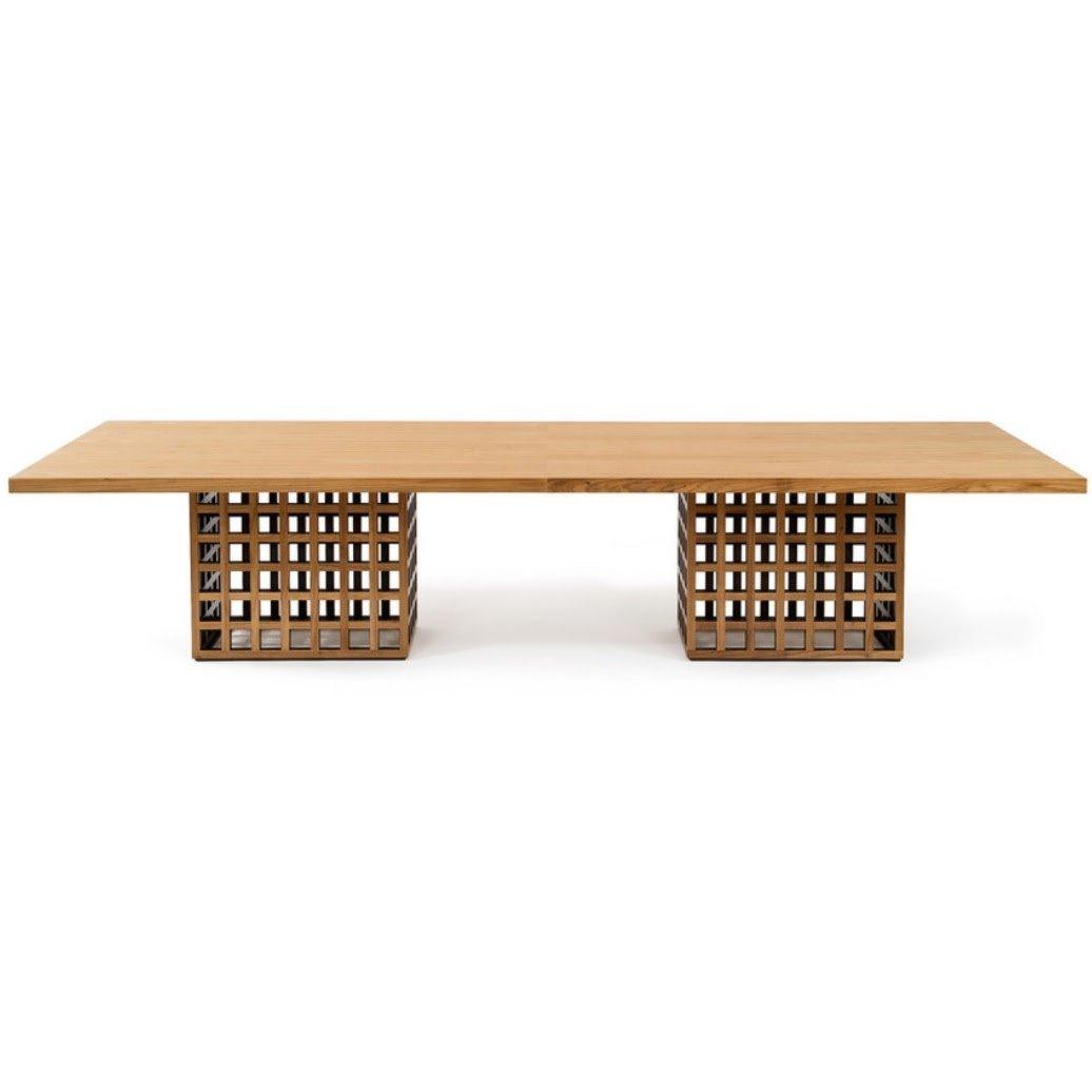 Long rectangular dining table in natural oak with a slim solid-wood top supported by two cube-shaped lattice pedestal bases, modern minimalist design.