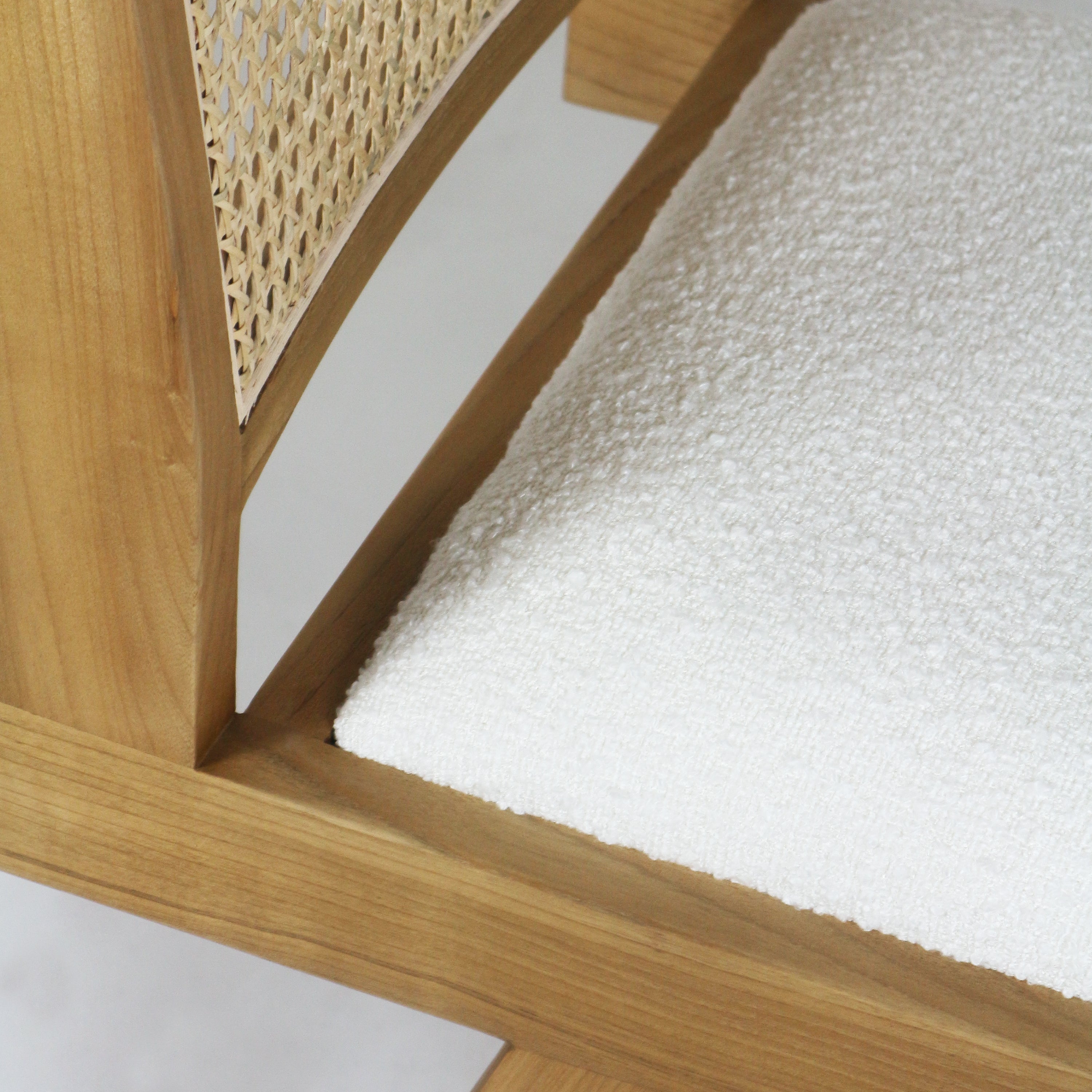 Close-up of a natural blonde wood armless side chair showing a woven cane back and a cream boucle upholstered seat with textured fabric and visible wood grain.