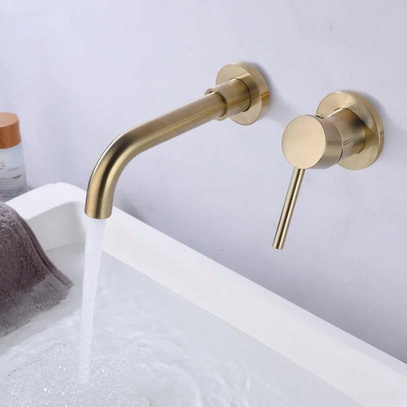 Brushed brass wall-mounted bathroom faucet and single-lever mixer tap with water flowing into a white bathtub.