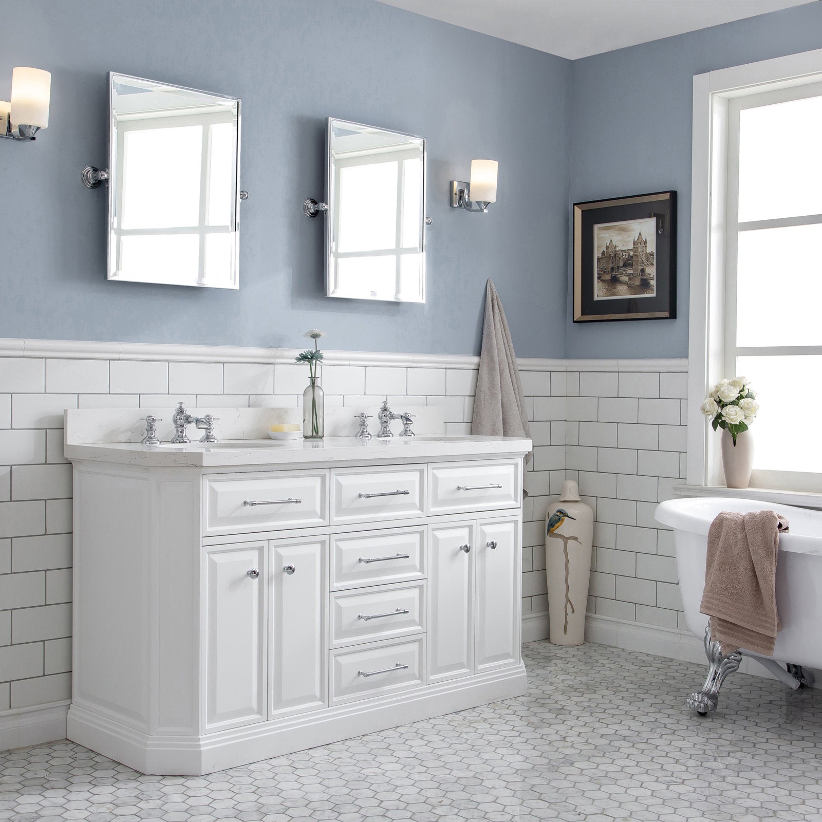 Freestanding white solid-wood bathroom vanity with stone countertop, chrome faucets and drawer hardware, subway-tile backsplash, twin mirrors and sconces, hex-tile floor and a clawfoot tub in a soft-blue bathroom.
