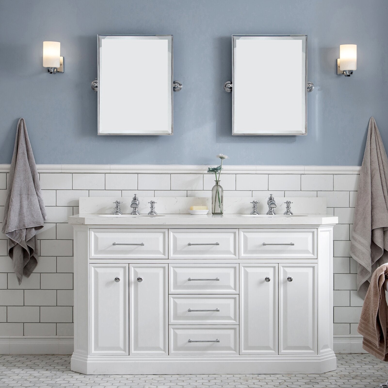 White 60-inch modern solid wood freestanding bathroom vanity with a stone countertop and double ceramic sinks, chrome faucets and hardware, center drawers and cabinets; styled with two mirrors, sconces, subway tile and gray towels.