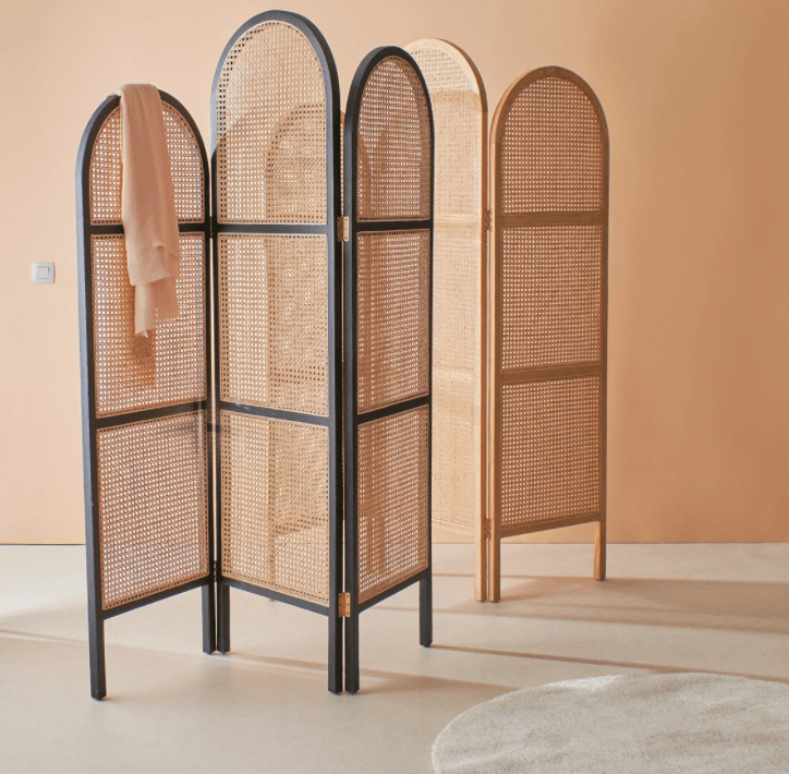 Four-panel solid wood and rattan folding room divider with arched tops, two black-framed panels and two natural wood panels featuring cane weave, styled in a warm neutral room with a light scarf draped on one panel.